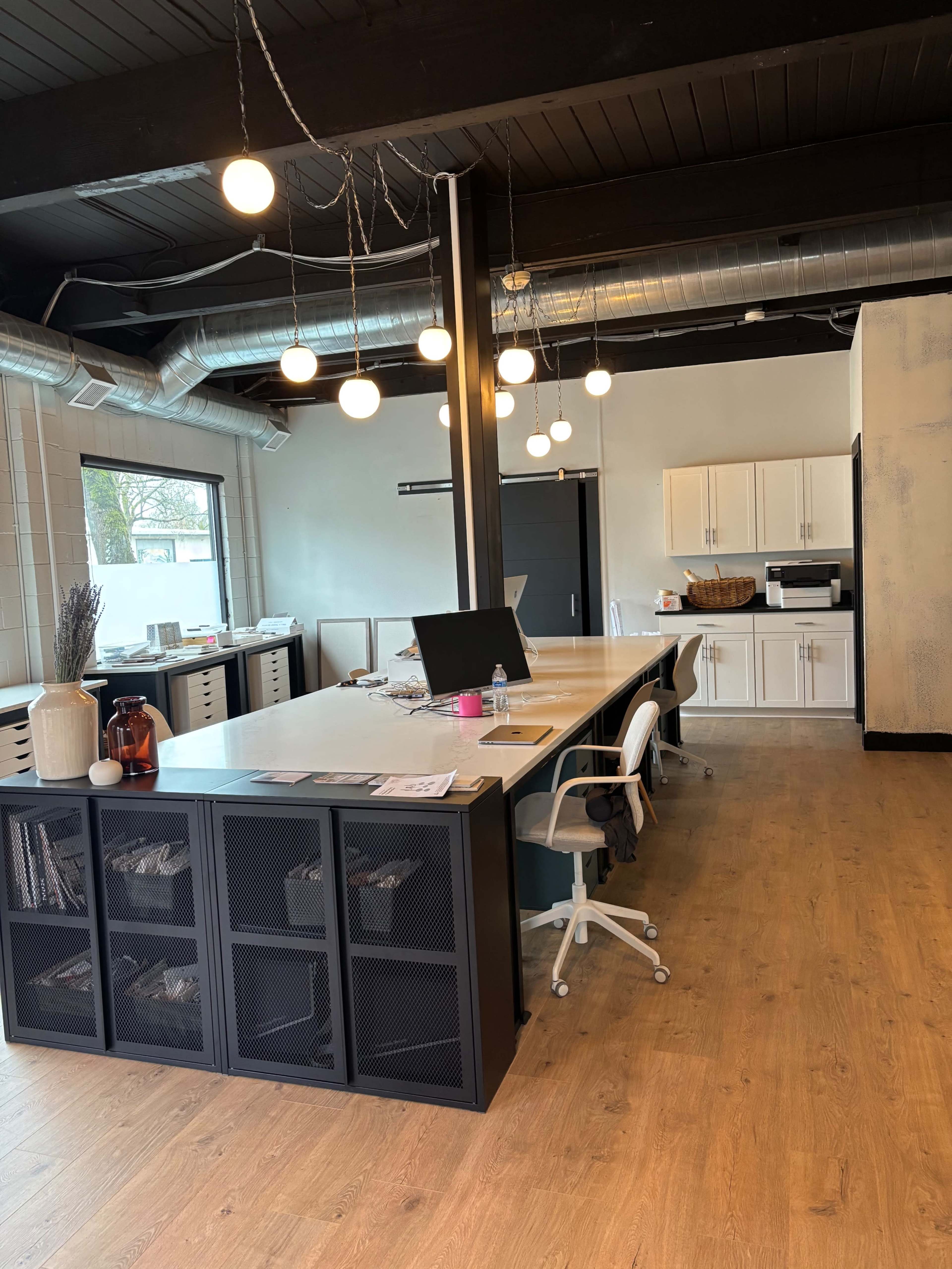 The image shows a modern office space with a large central table, chairs, and storage units, featuring sleek design elements and ambient lighting.