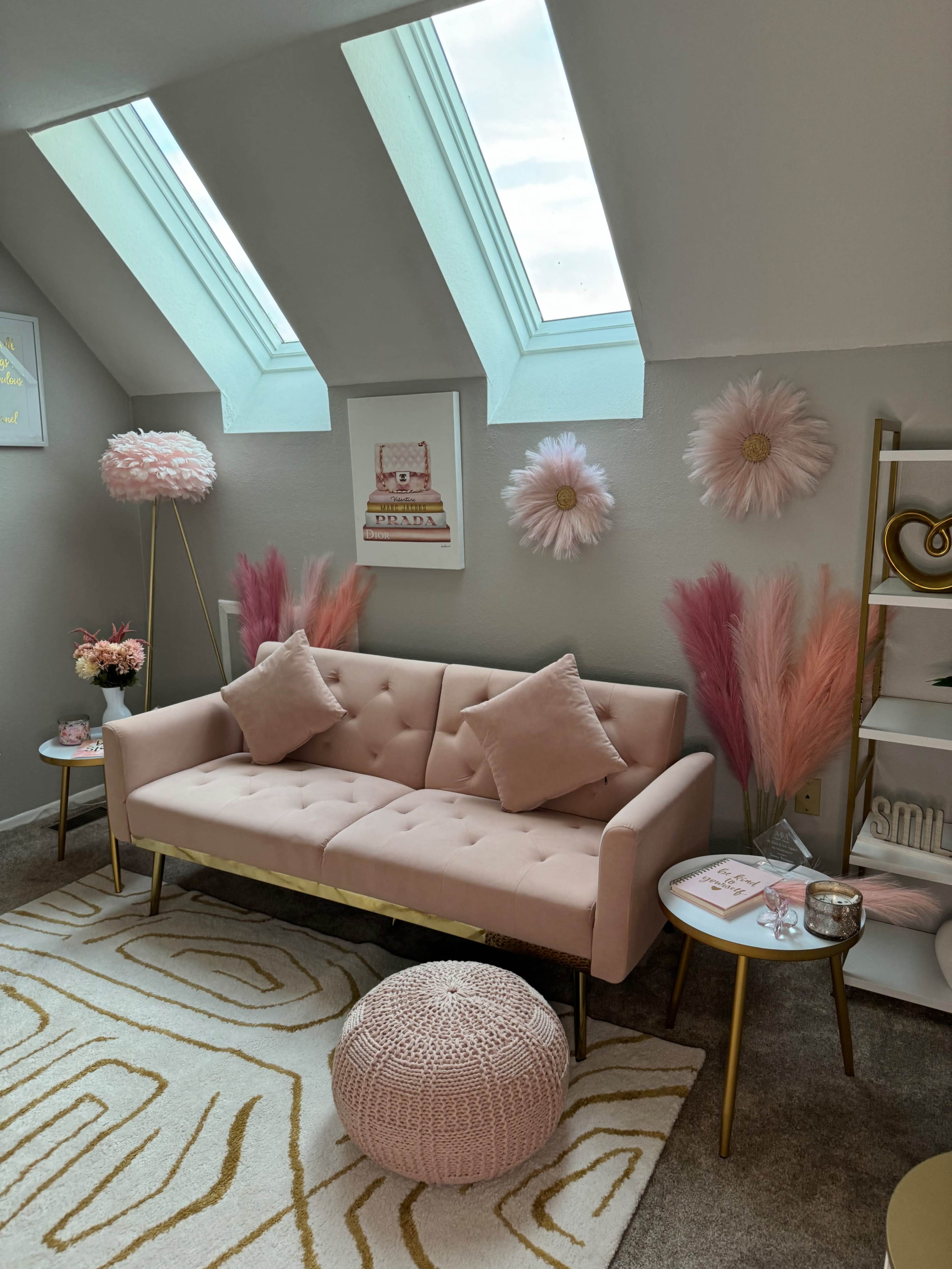 The image shows a cozy living space featuring a pink tufted sofa, decorative wall hangings, and a mix of plants and furnishings in soft pastel tones.