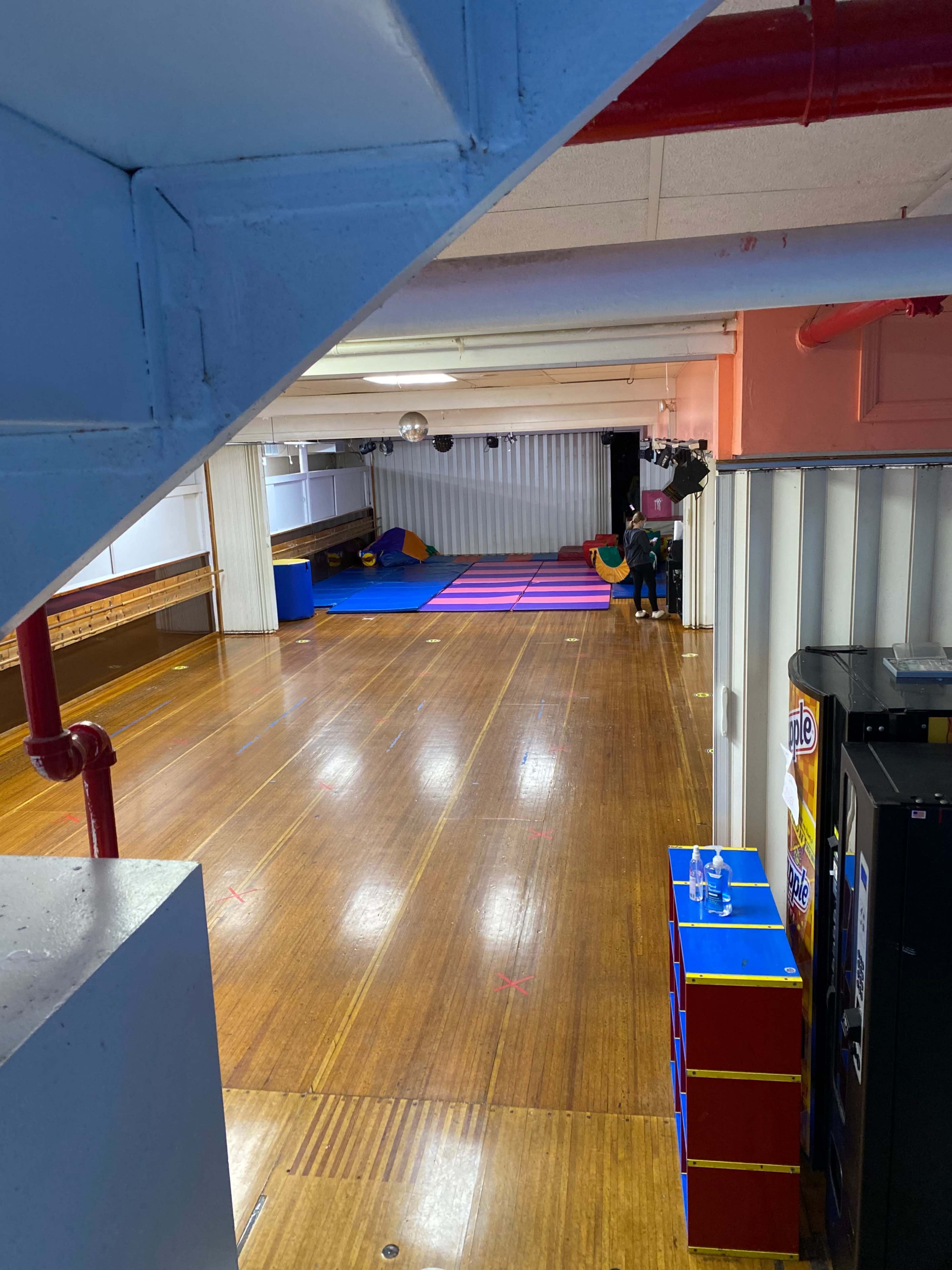 A spacious wooden-floored room with colorful mats in the background and a vending machine on the left side.