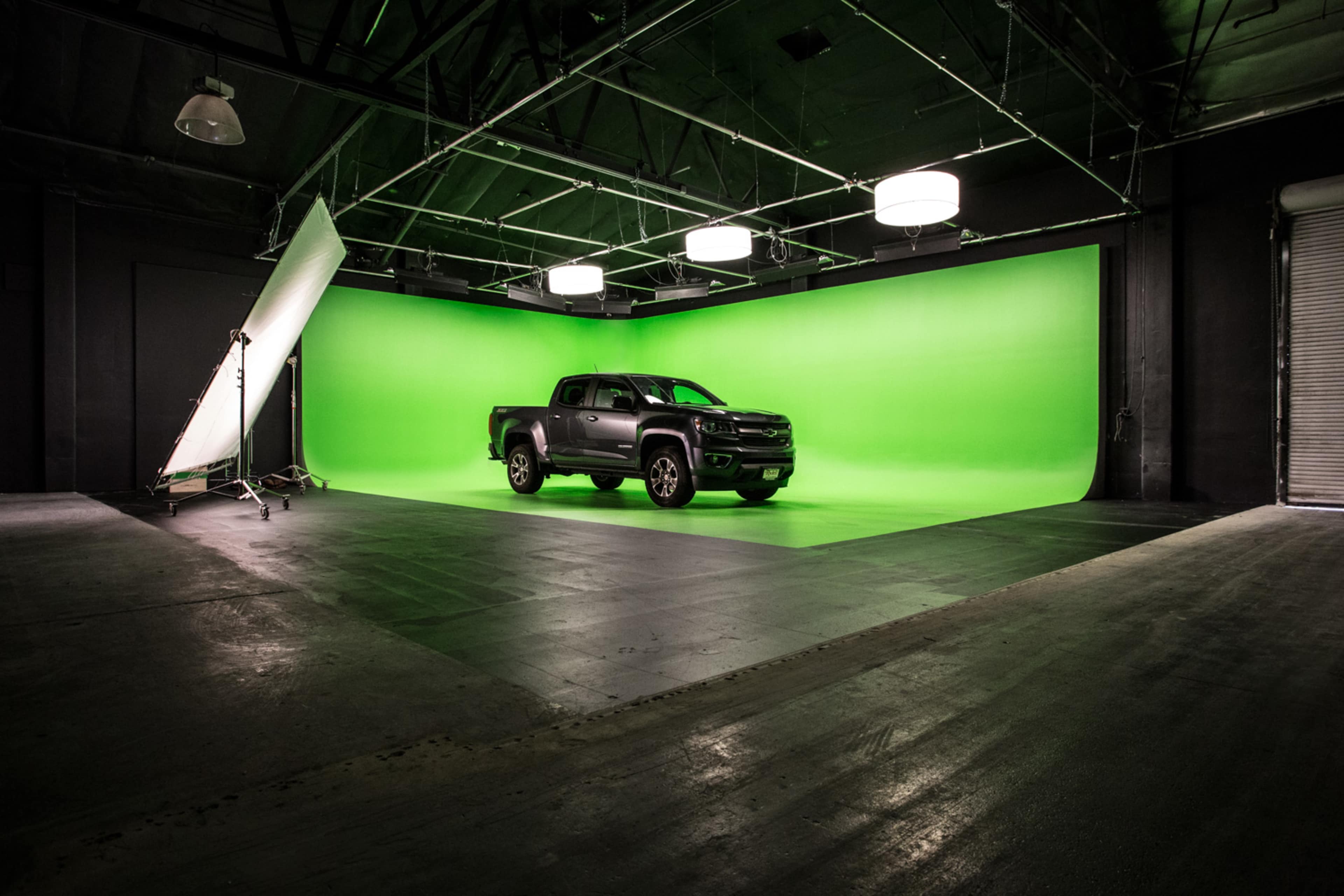 A black pickup truck is centered on a green screen backdrop in a spacious studio with industrial lighting.