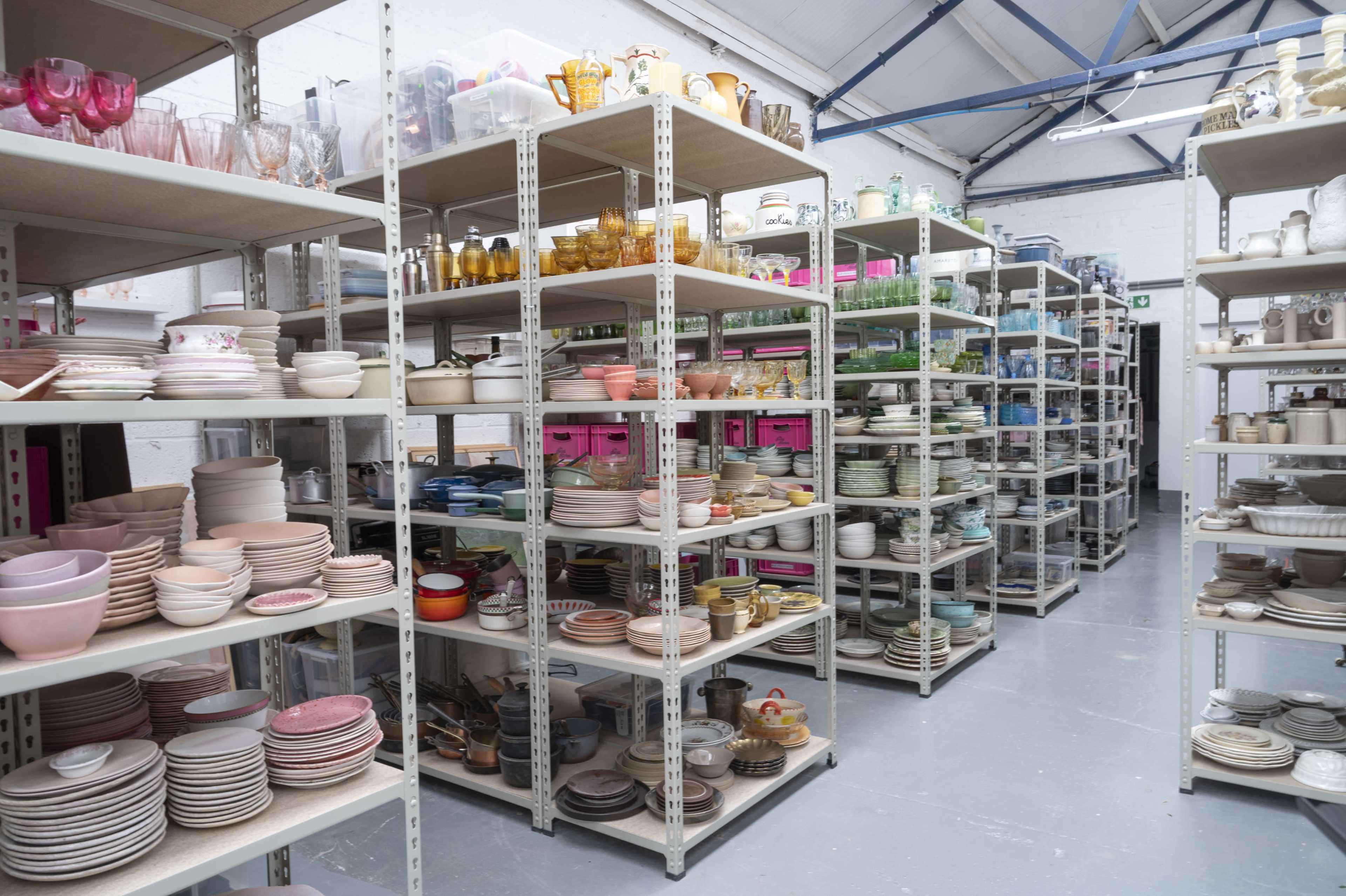 A neatly organized warehouse filled with shelves displaying an assortment of kitchenware, including plates, bowls, and glasses.