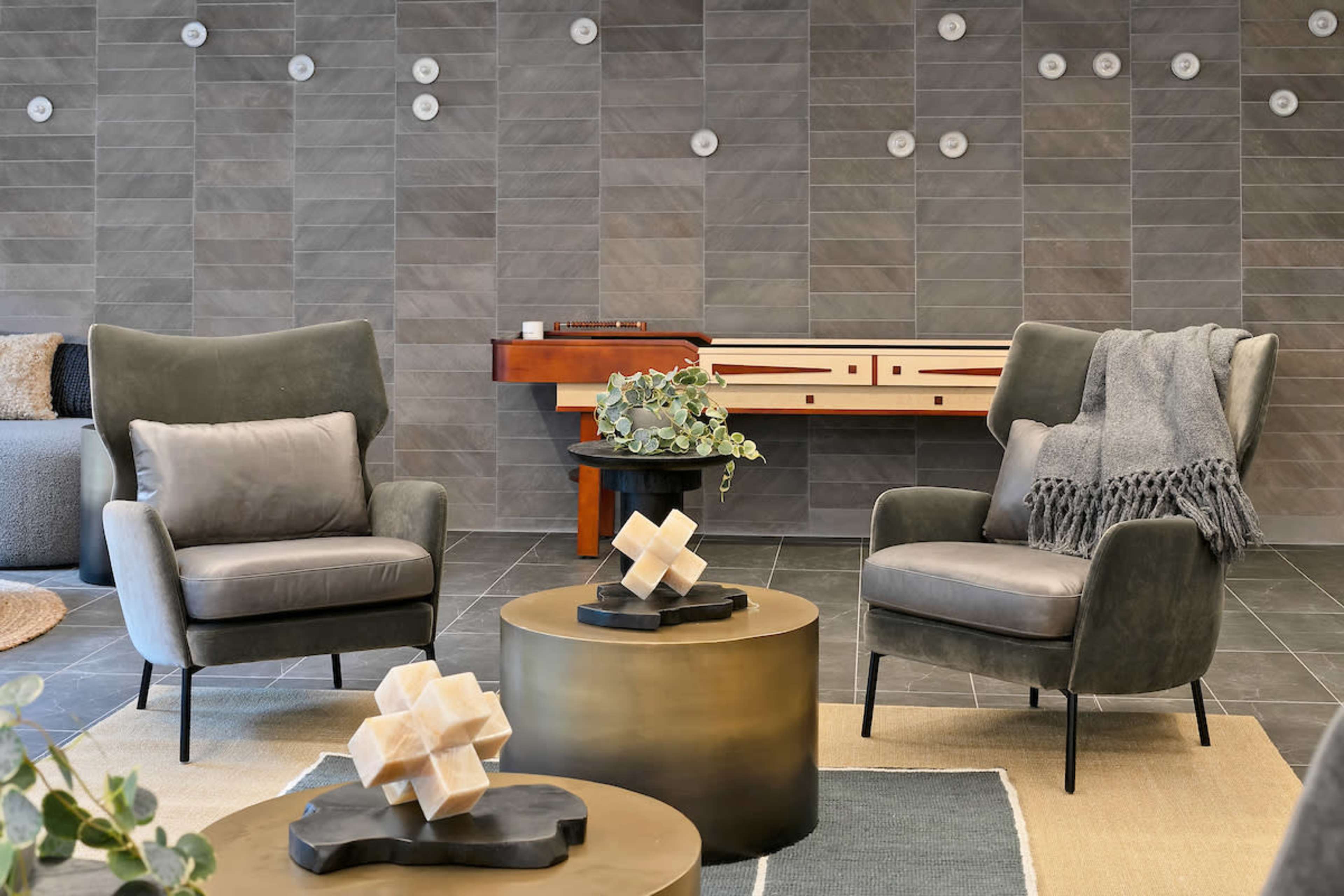 A modern interior with two gray armchairs, a round coffee table, and a decorative wooden console against a tile wall.