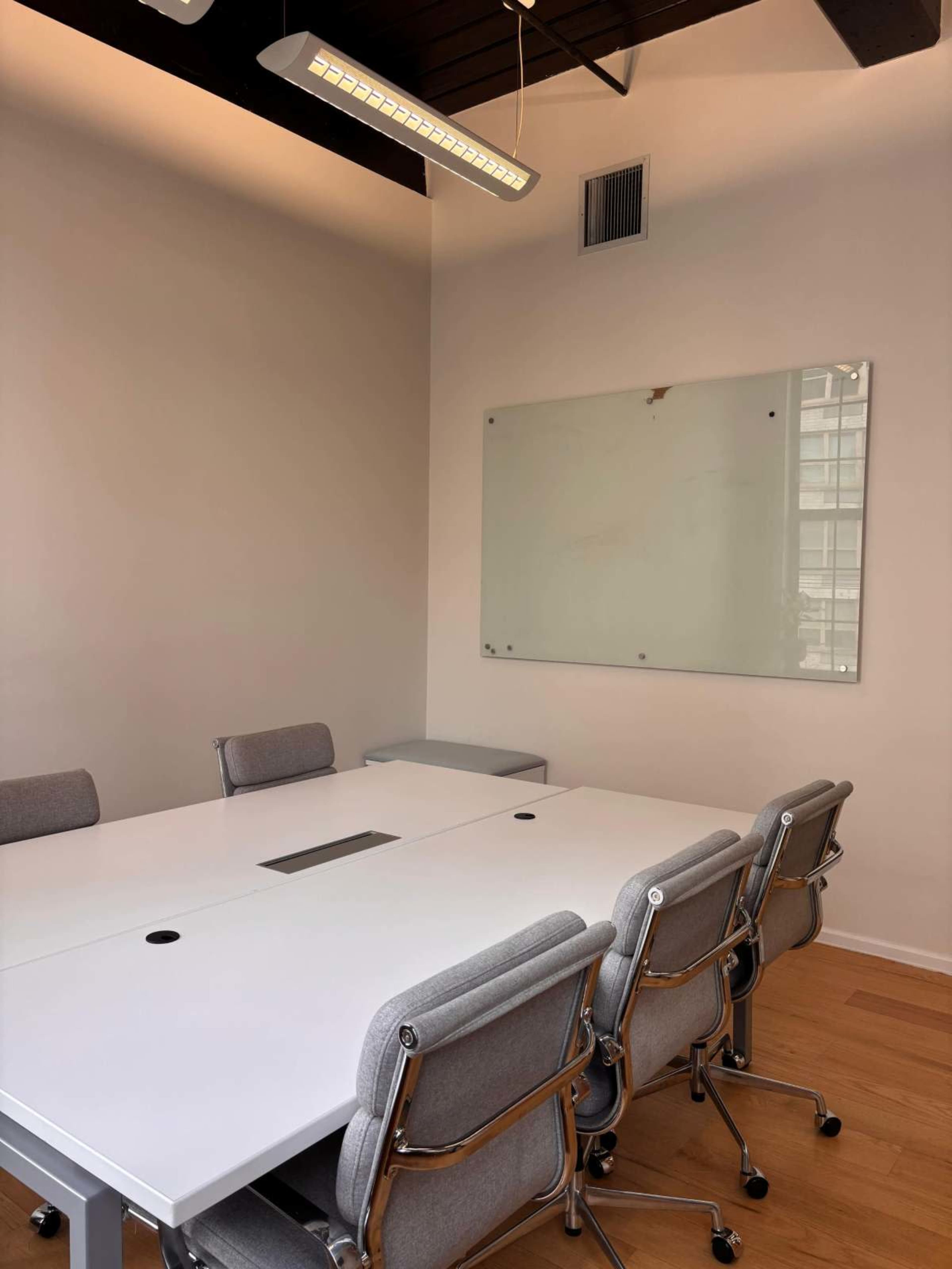A modern conference room features a large rectangular table surrounded by sleek chairs, with a whiteboard mounted on the wall and overhead lighting.