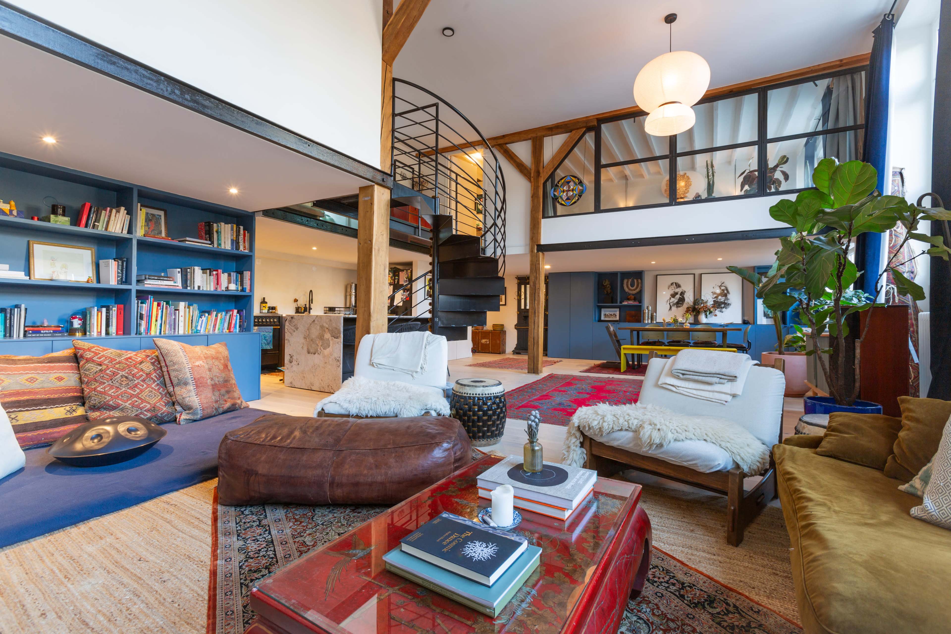A stylish, open-concept living space featuring a spiral staircase, bookshelves filled with various books, and a seating area with a mix of cozy furniture and decorative elements.