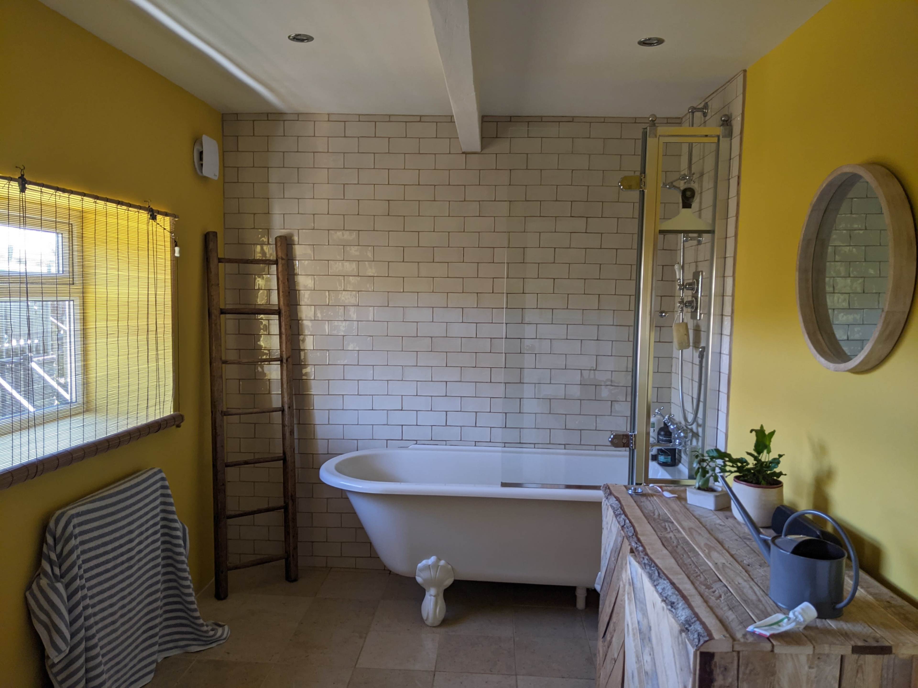 A bathroom with a freestanding bathtub, a wooden ladder, and a large mirror on a yellow wall.