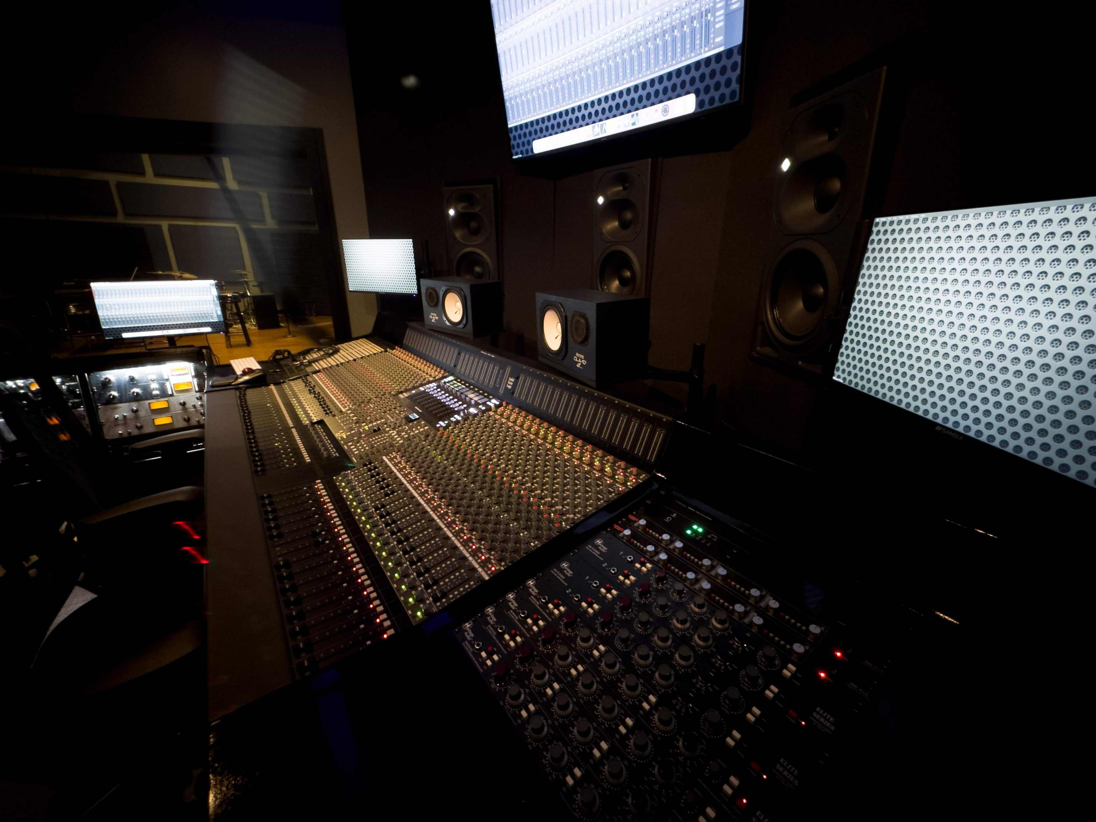 A professional audio mixing console surrounded by multiple monitors in a sound studio.