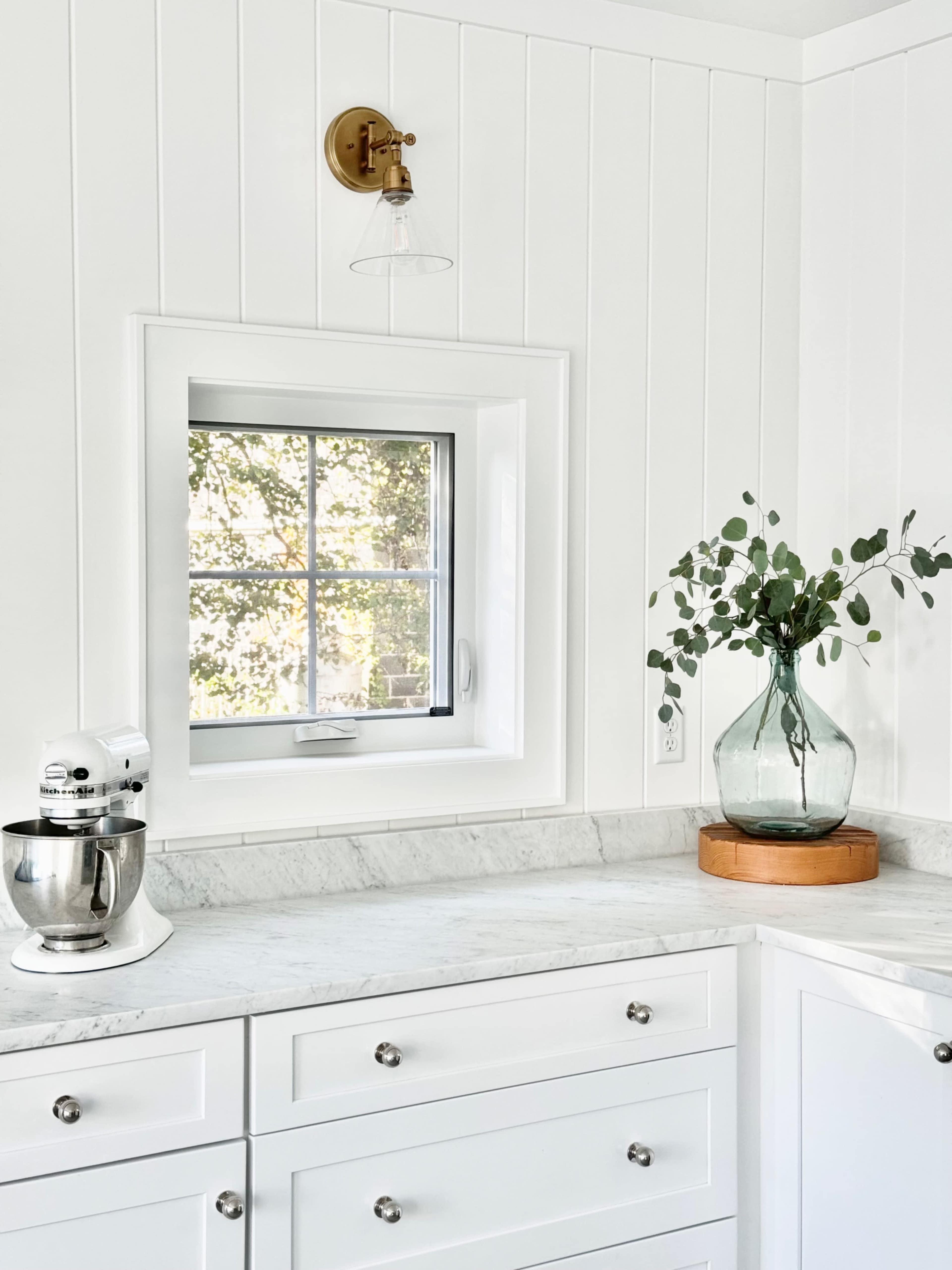 A kitchen corner features a marble countertop with a stand mixer, a glass vase with greenery, and a window providing natural light.