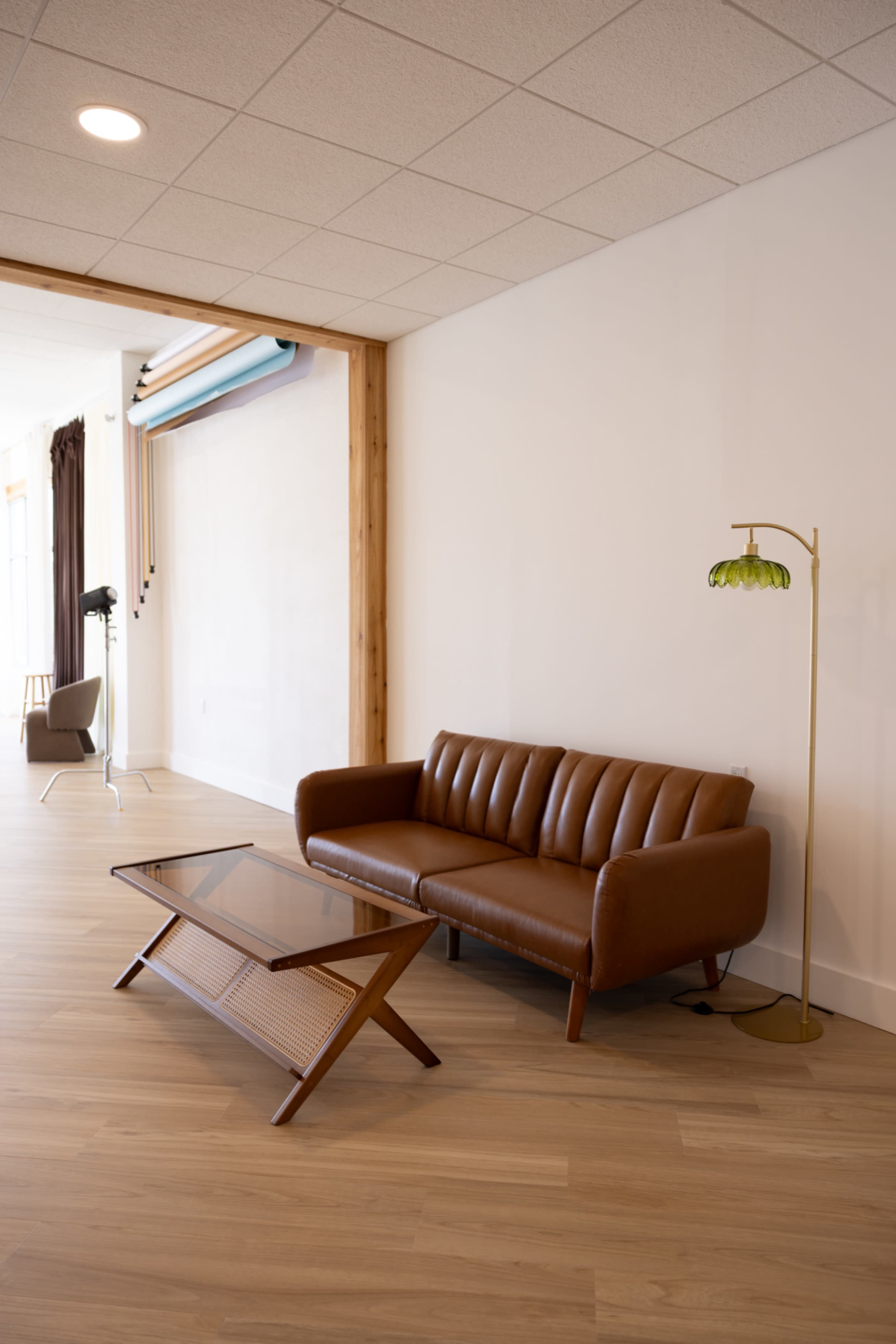 The image shows a modern interior space featuring a brown leather sofa, a glass coffee table, and a floor lamp with a green shade.