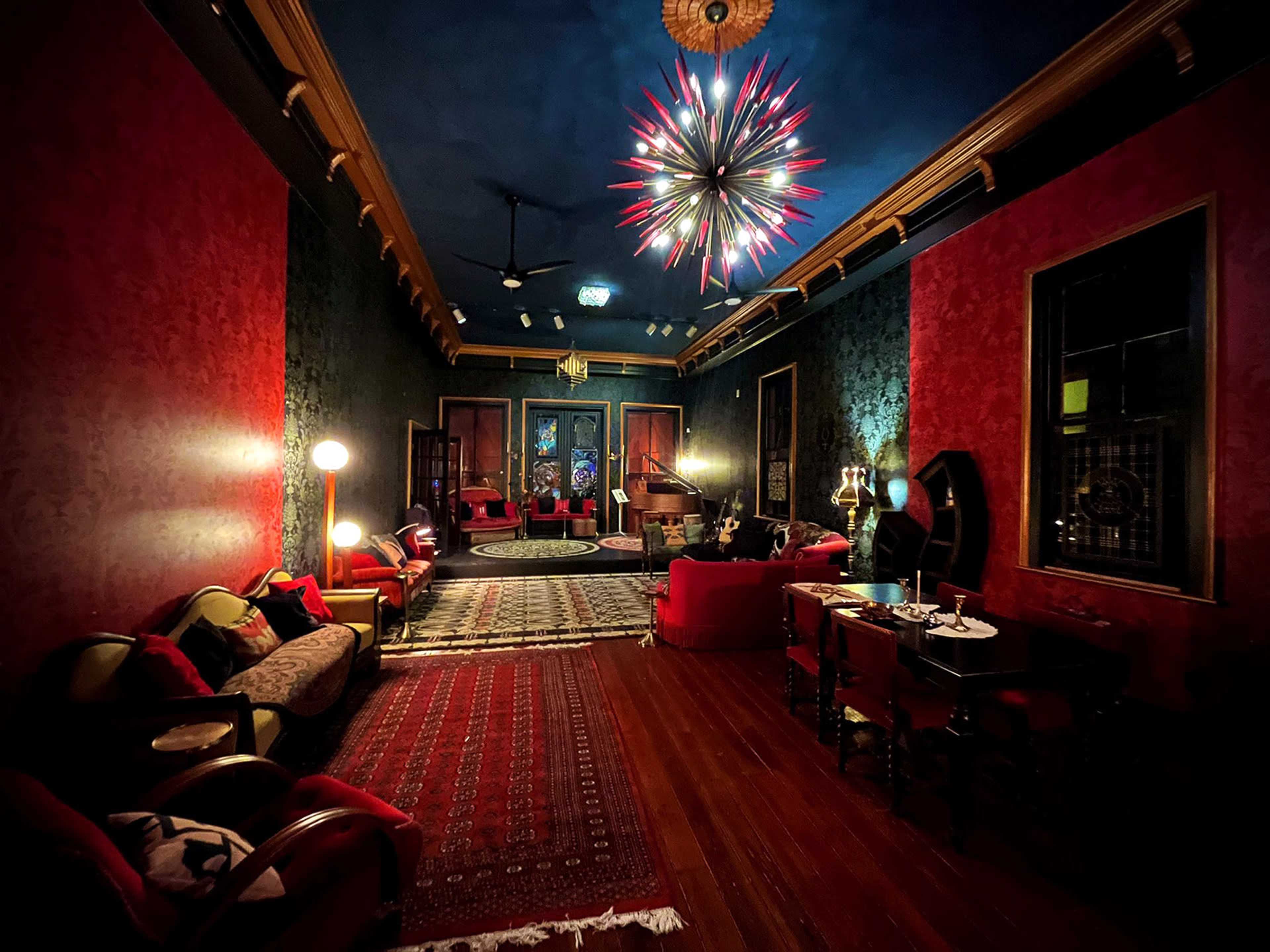 A dimly lit room furnished with red sofas, a patterned rug, and a decorative ceiling light, creating an intimate atmosphere.