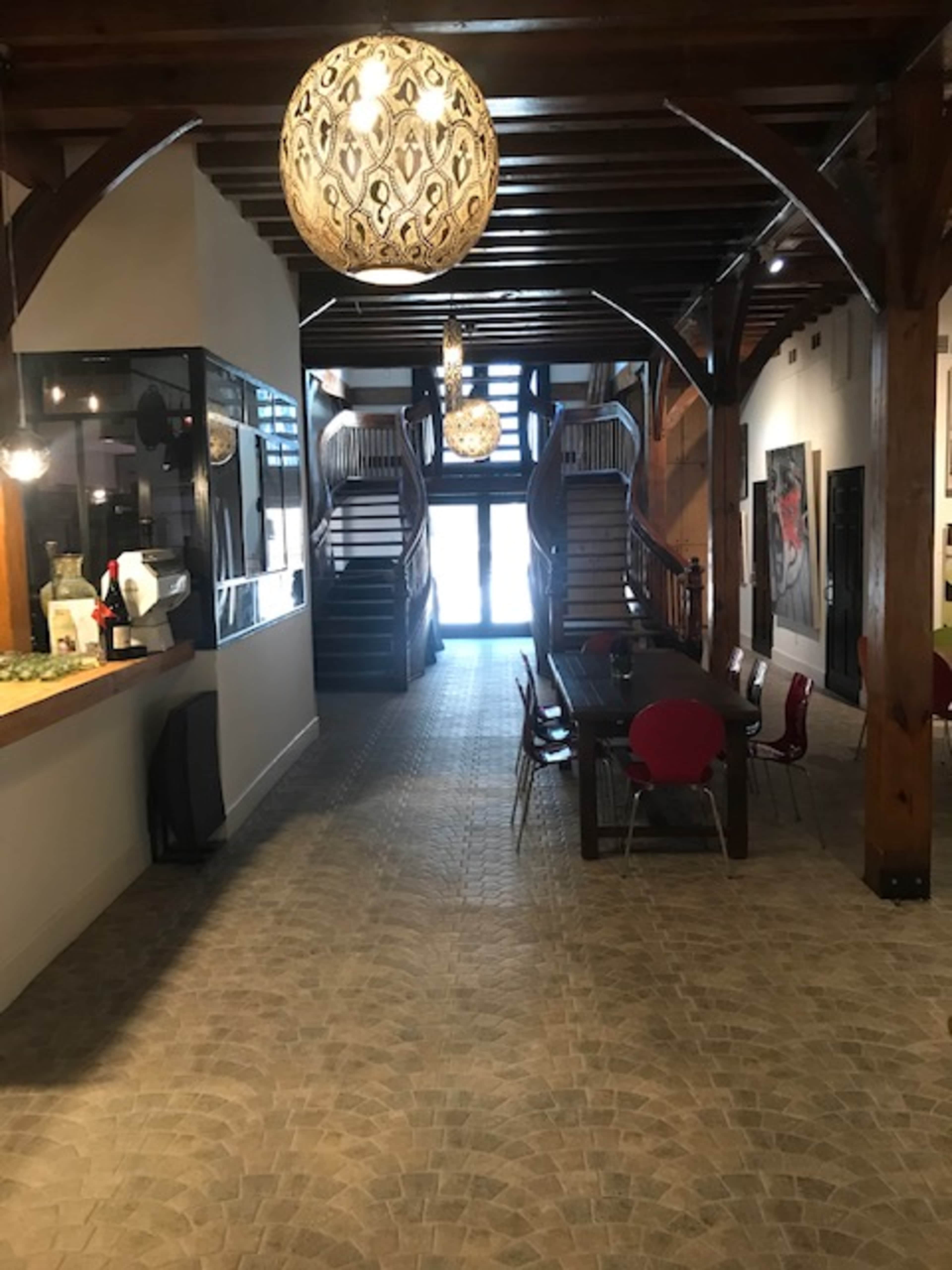 A spacious hallway with wooden beams, two staircases leading to an upper level, and a long dining table surrounded by red chairs.