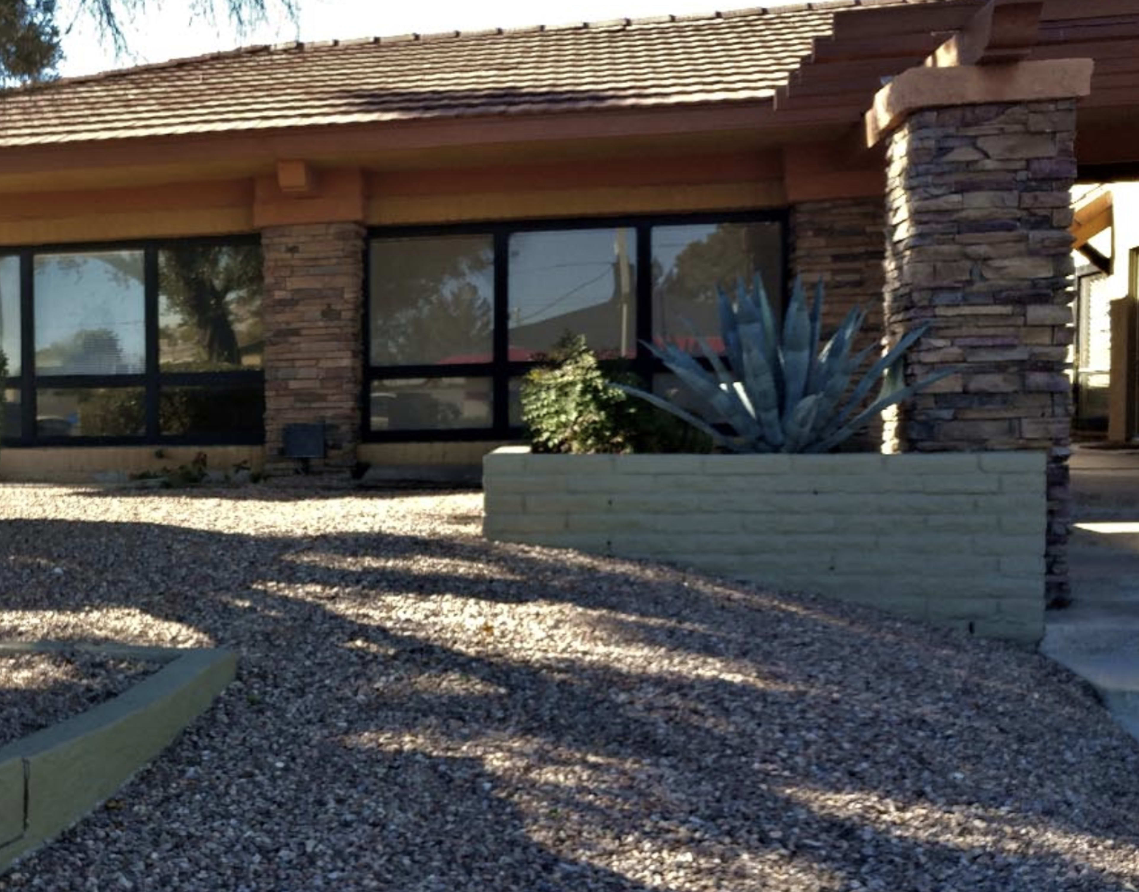 A house with a stone exterior, large windows, and a landscaped front yard featuring gravel and a planter with an agave plant.