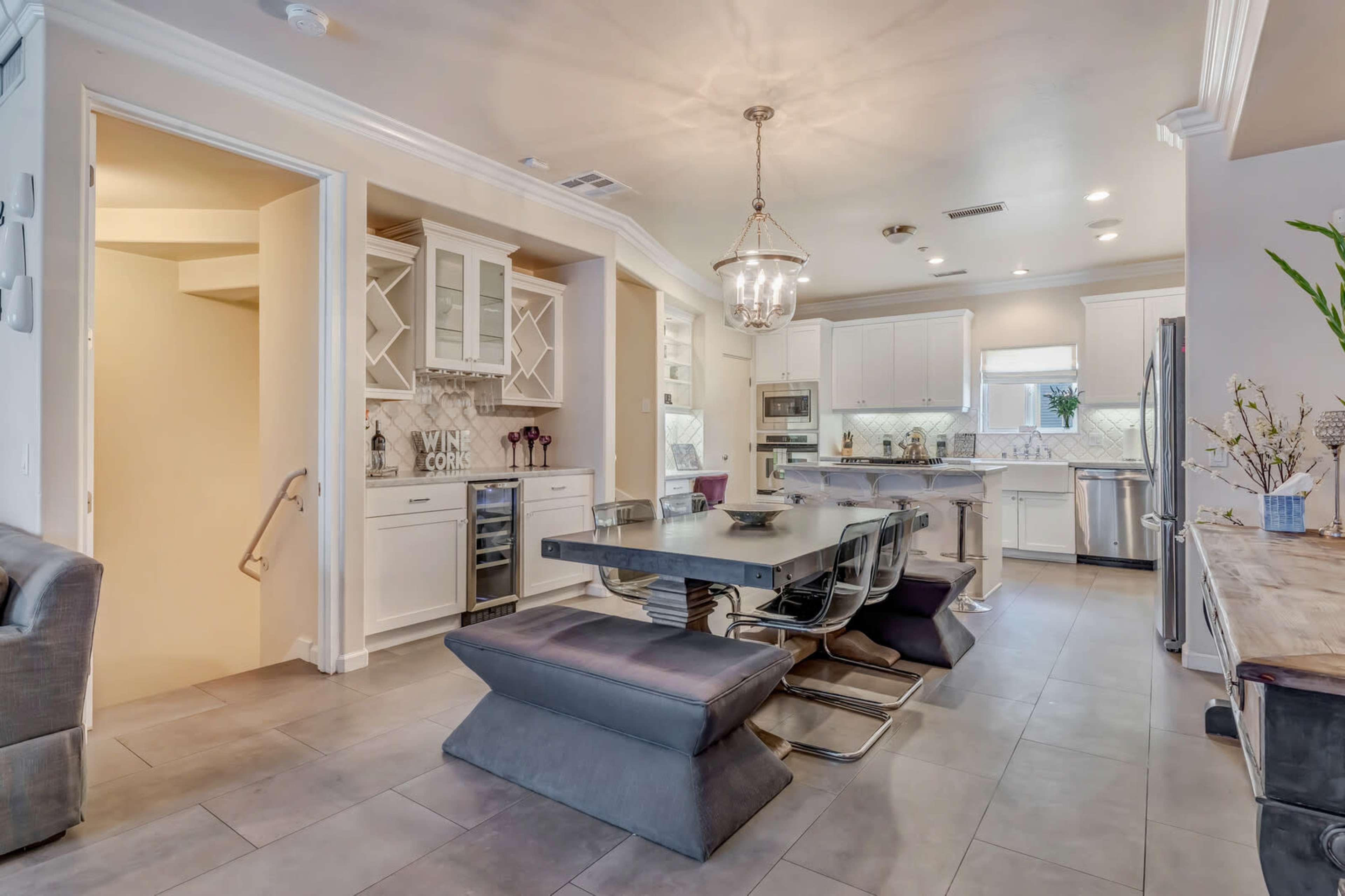 A modern kitchen and dining area with a sleek dining table, black chairs, and white cabinetry, featuring a wine cooler in a built-in nook.