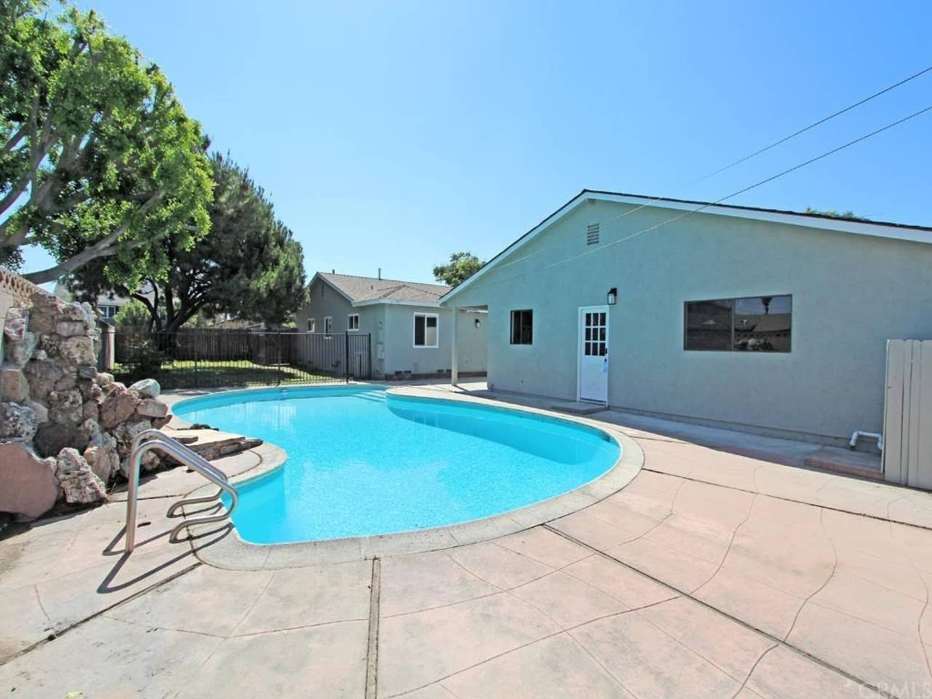 A swimming pool surrounded by a concrete patio and a single-story house in the background.