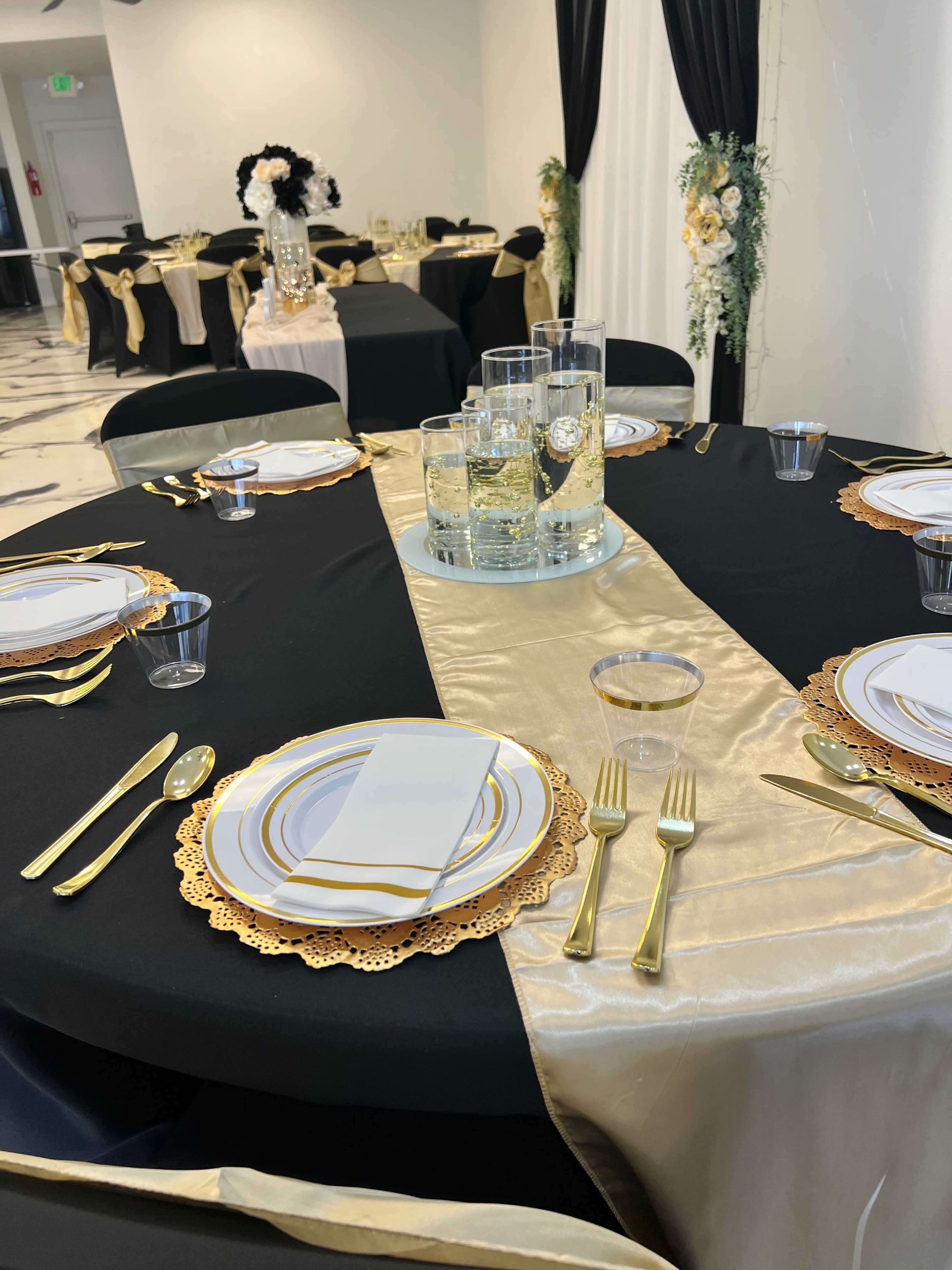 A dining setup with black and gold tables, each featuring elegant place settings with gold-accented plates and cutlery.
