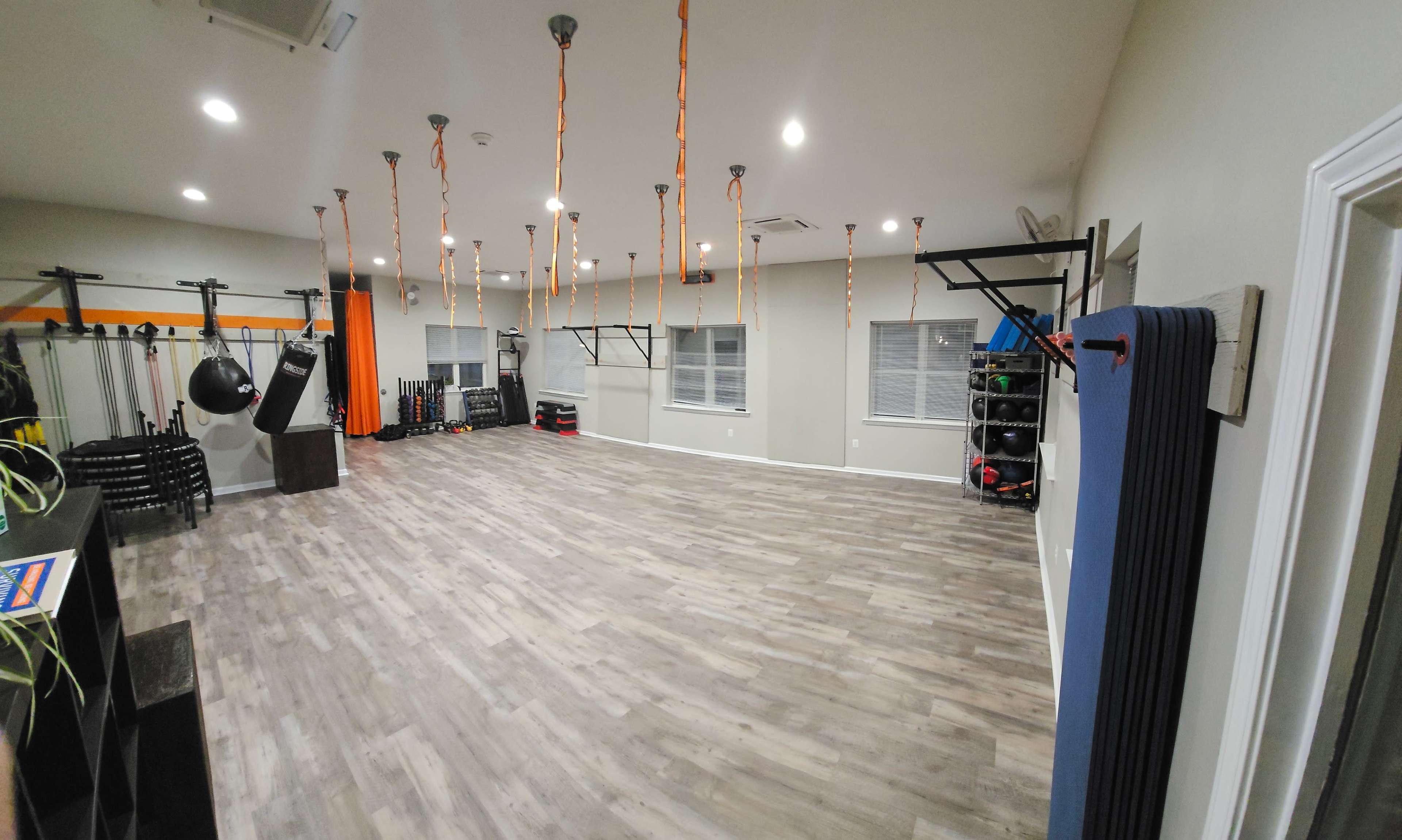 A spacious gym interior equipped with various fitness equipment, wall-mounted racks, and overhead hanging decorations.