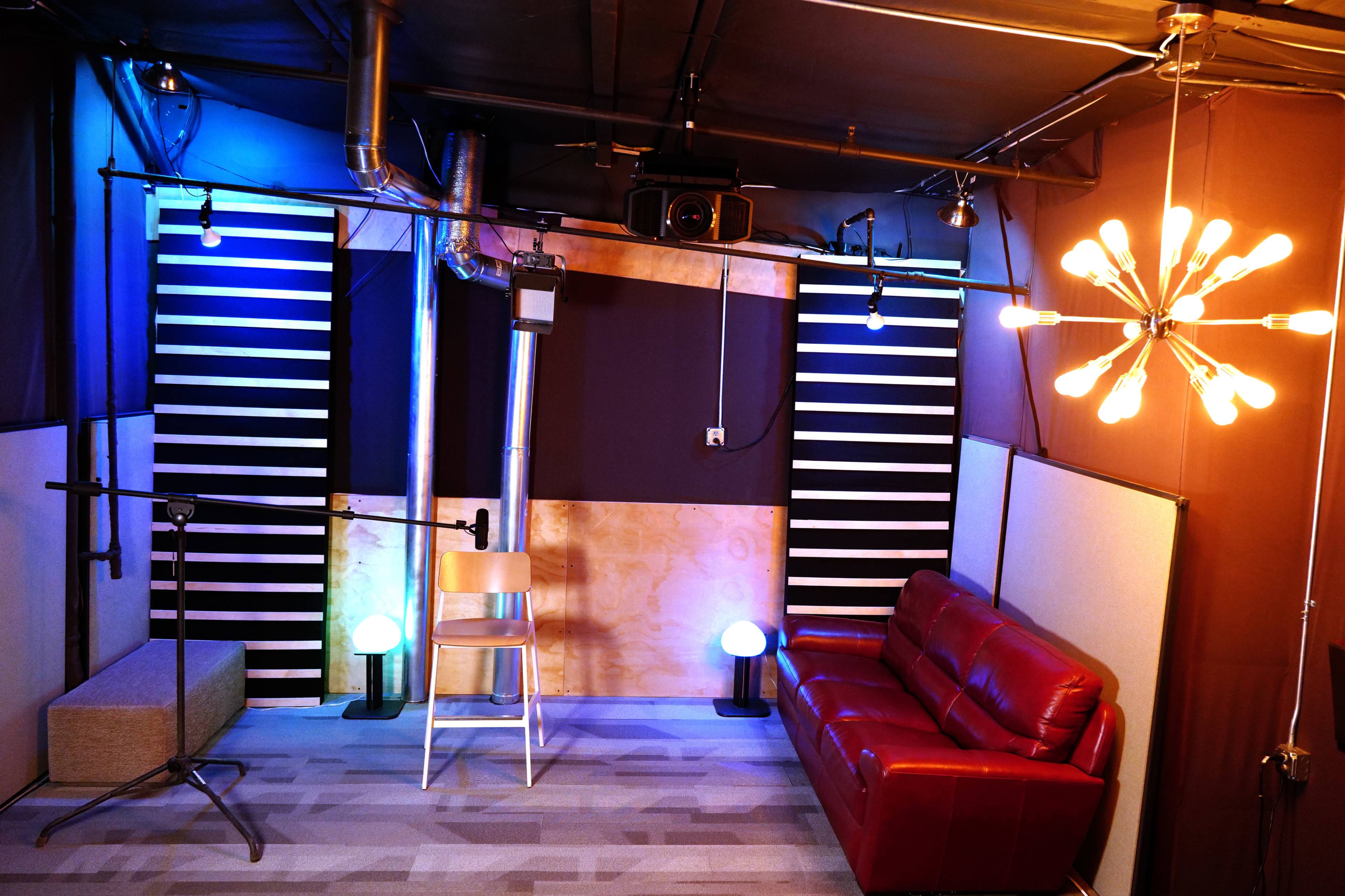 A small recording studio featuring a red couch, a microphone setup, and ambient lighting with a modern light fixture.