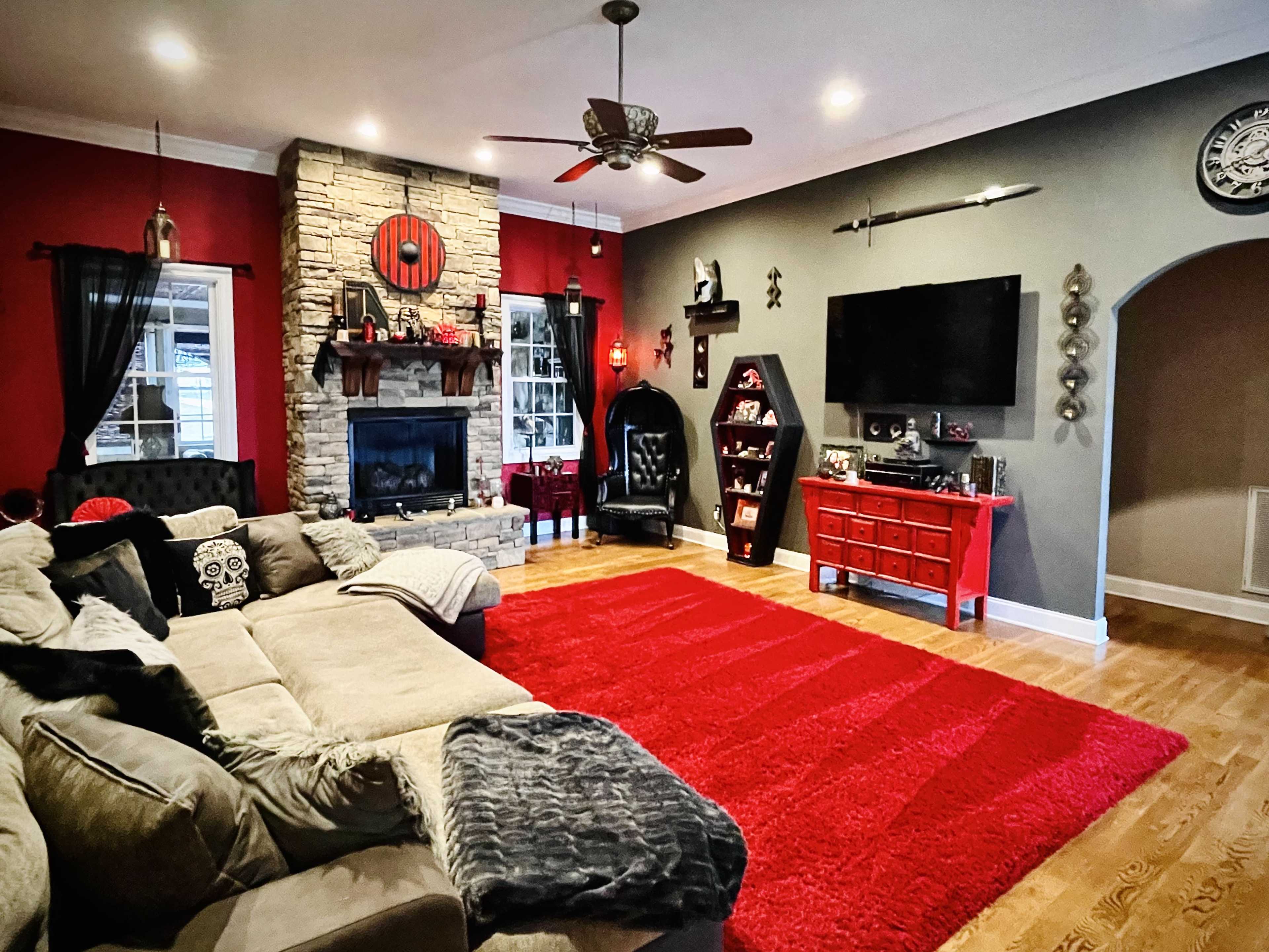 The living room features a large sectional sofa, a red area rug, a stone fireplace, and dark walls adorned with decorative elements.