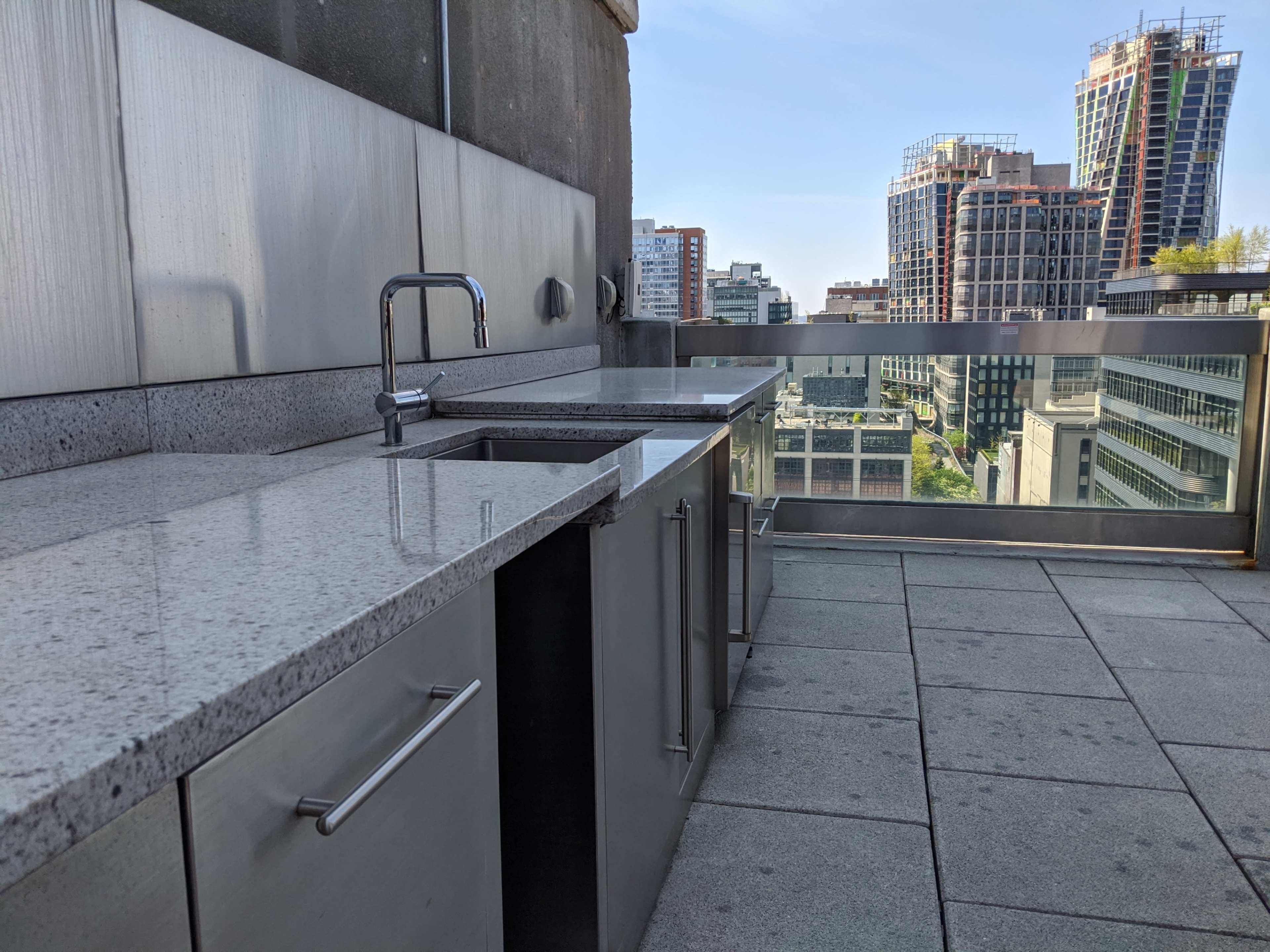 A modern outdoor kitchen with stainless steel cabinetry and a granite countertop, overlooking a city skyline.