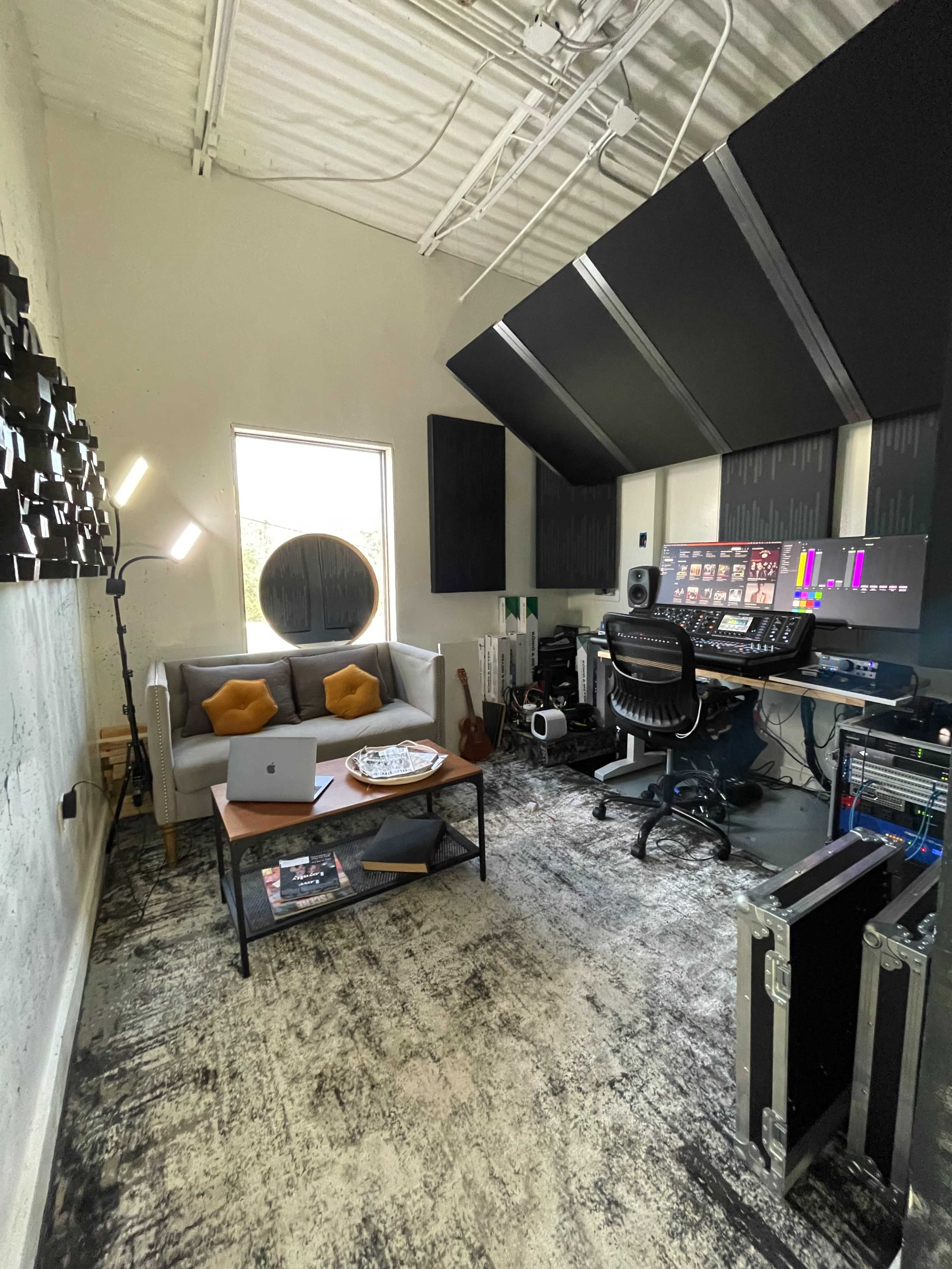 A music studio with a desk equipped with audio equipment, a comfortable seating area, and large soundproof panels on the walls.