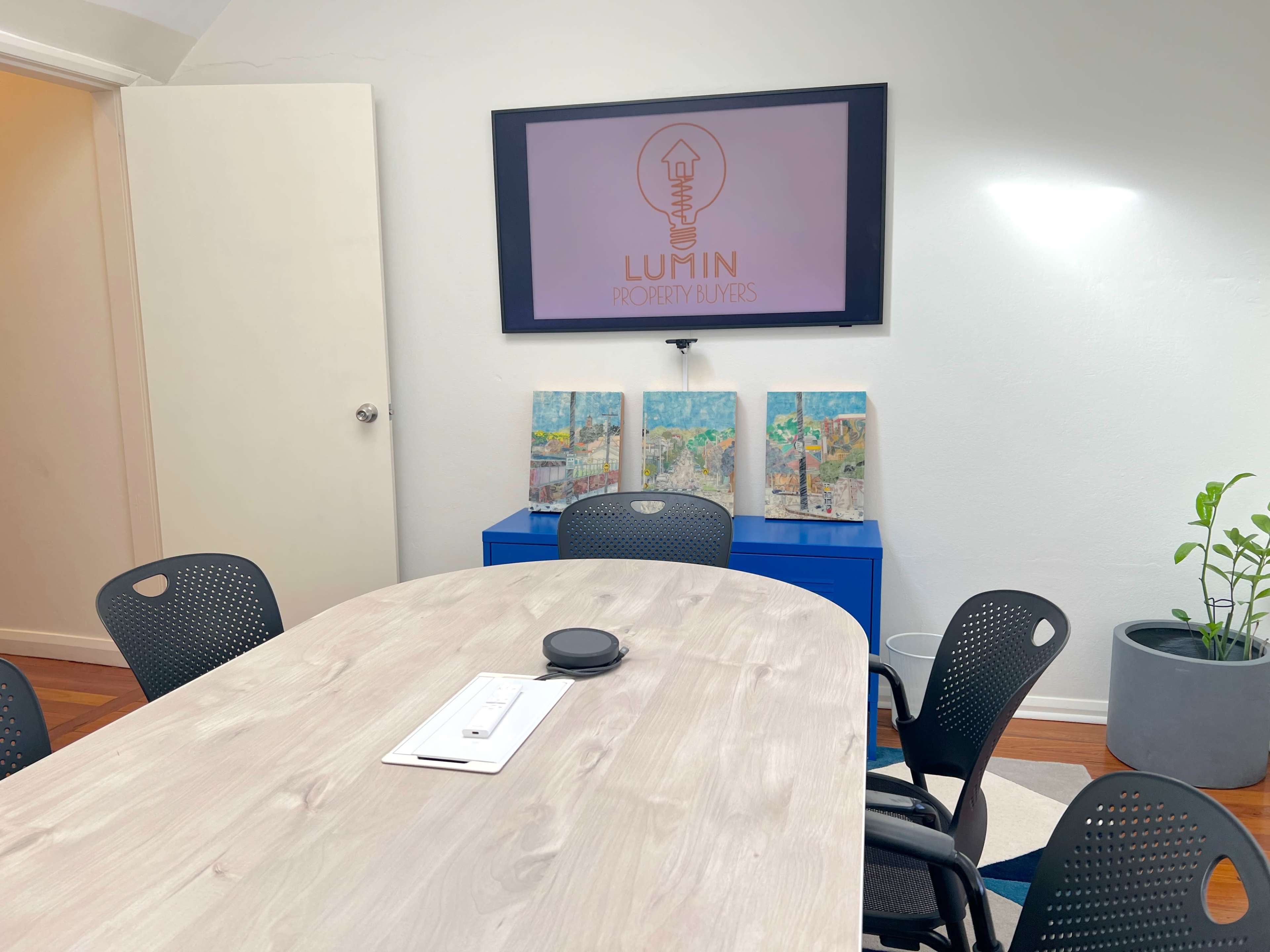 A conference room with a long table, a television displaying a logo, and decorative artwork on the wall.