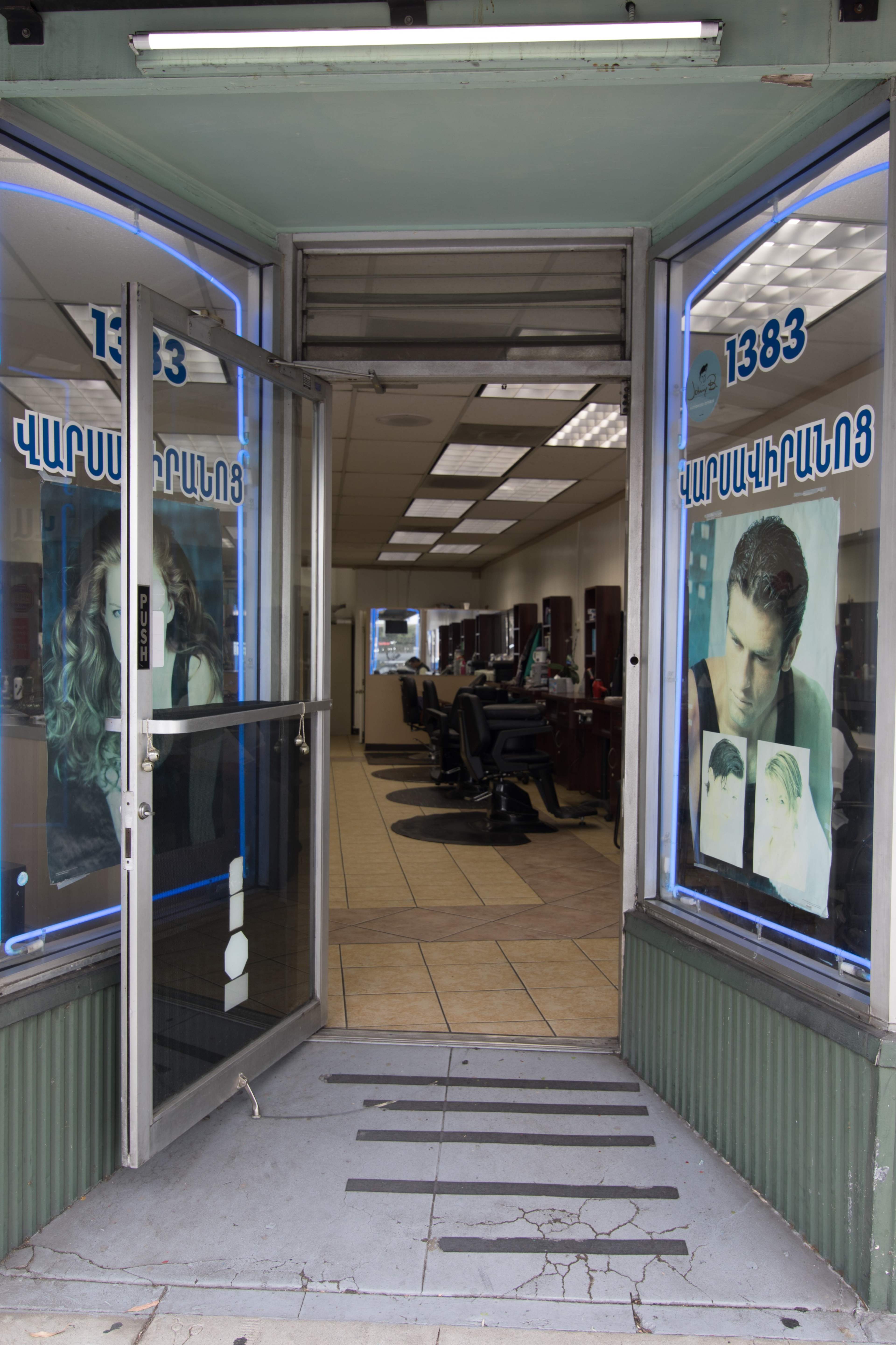 The entrance of a hair salon with large glass windows displaying posters of hairstyles, leading into a spacious interior with salon chairs.