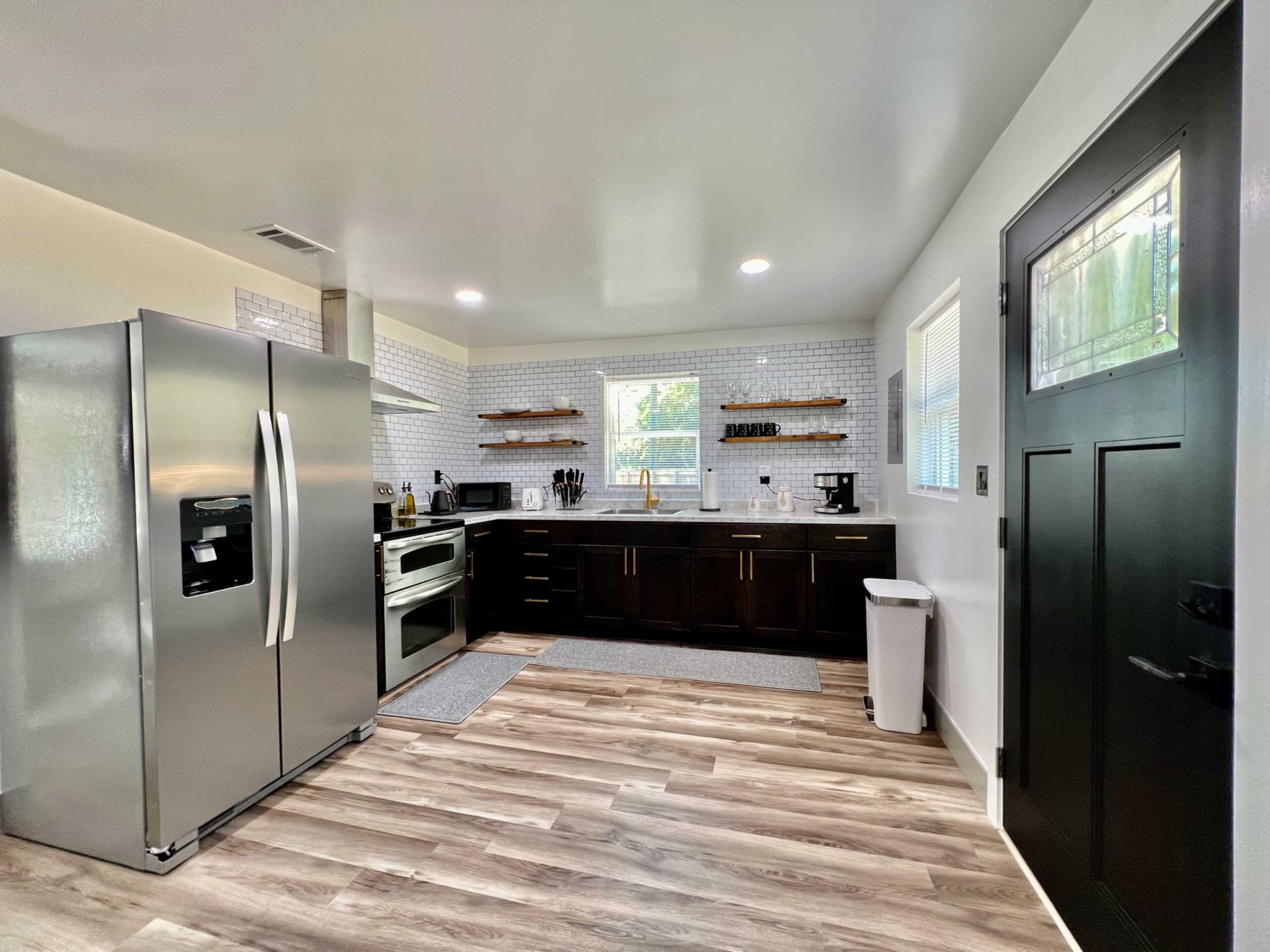 A modern kitchen equipped with stainless steel appliances, dark cabinetry, and light-colored walls, featuring a window that allows natural light to enter.
