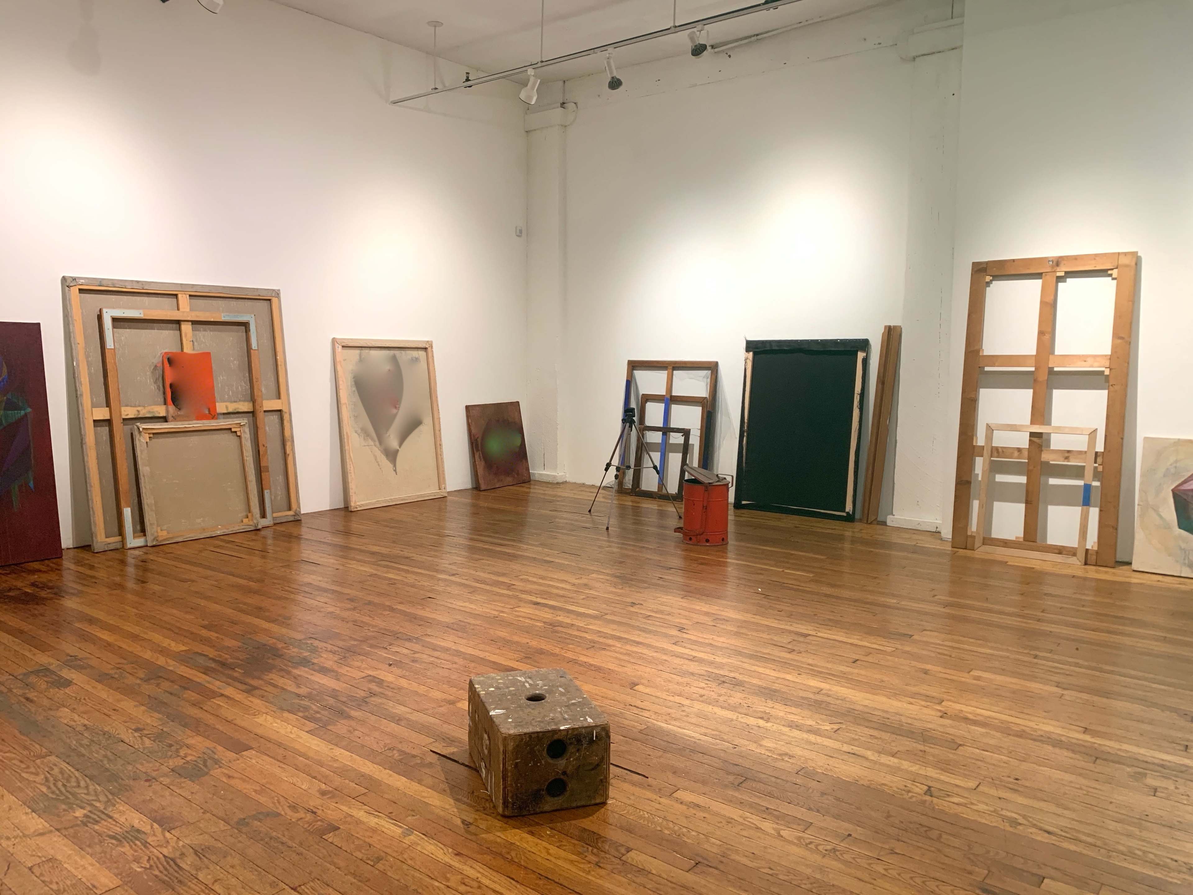 An art gallery featuring several framed artworks and wooden frames arranged on a wooden floor.