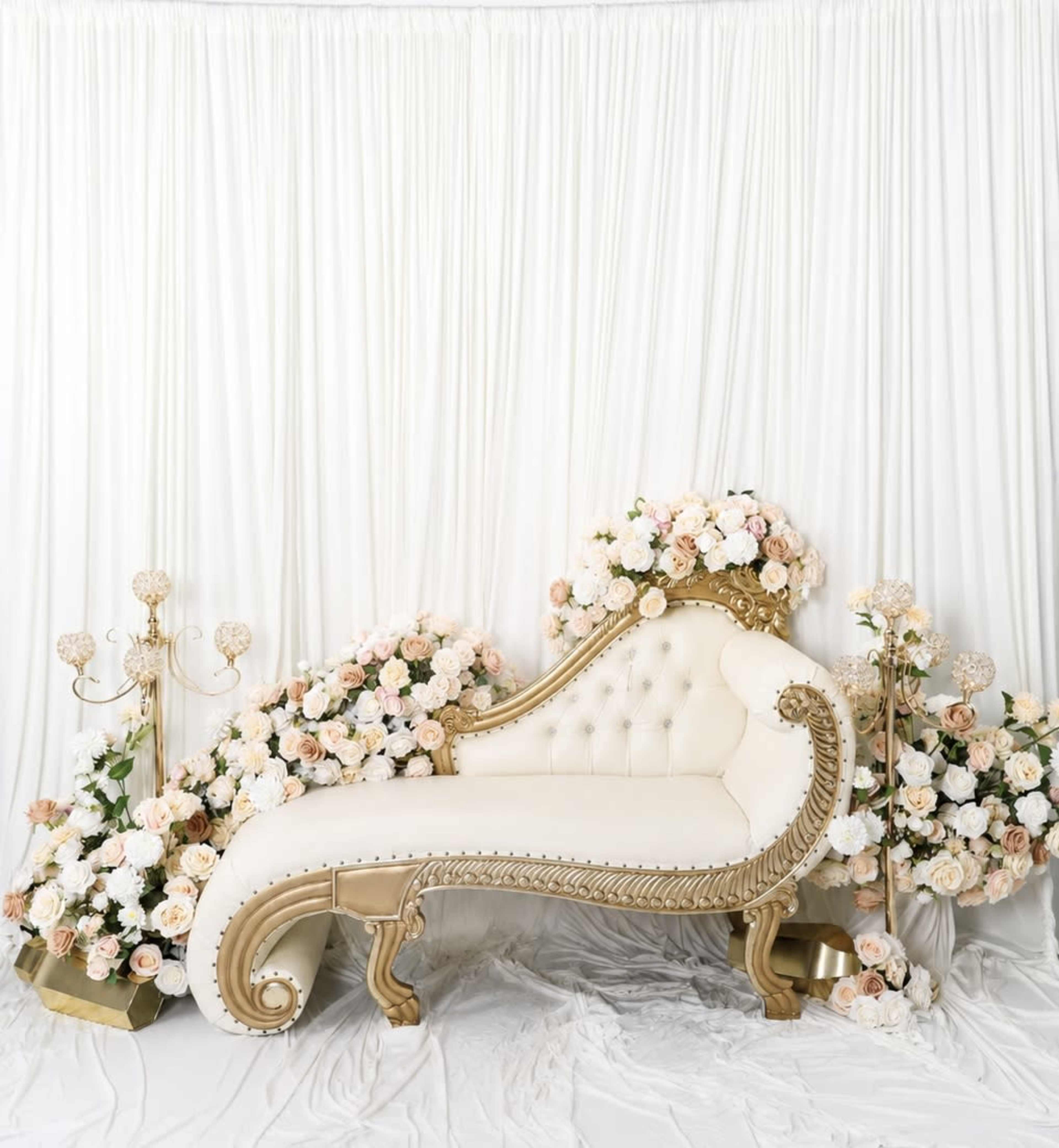 The image shows an elegant chaise lounge adorned with flowers against a backdrop of white fabric.
