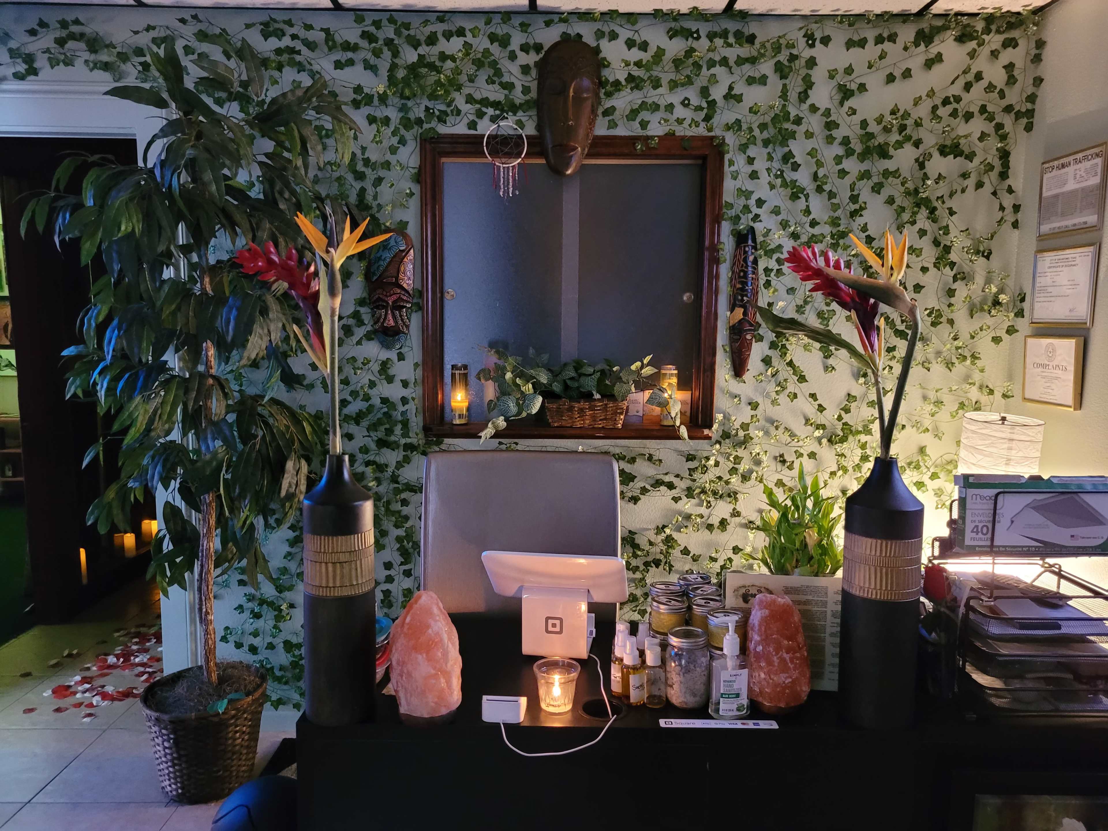 A tranquil spa-like setting with a desk adorned with candles, crystals, and decorative plants against a backdrop of green foliage.