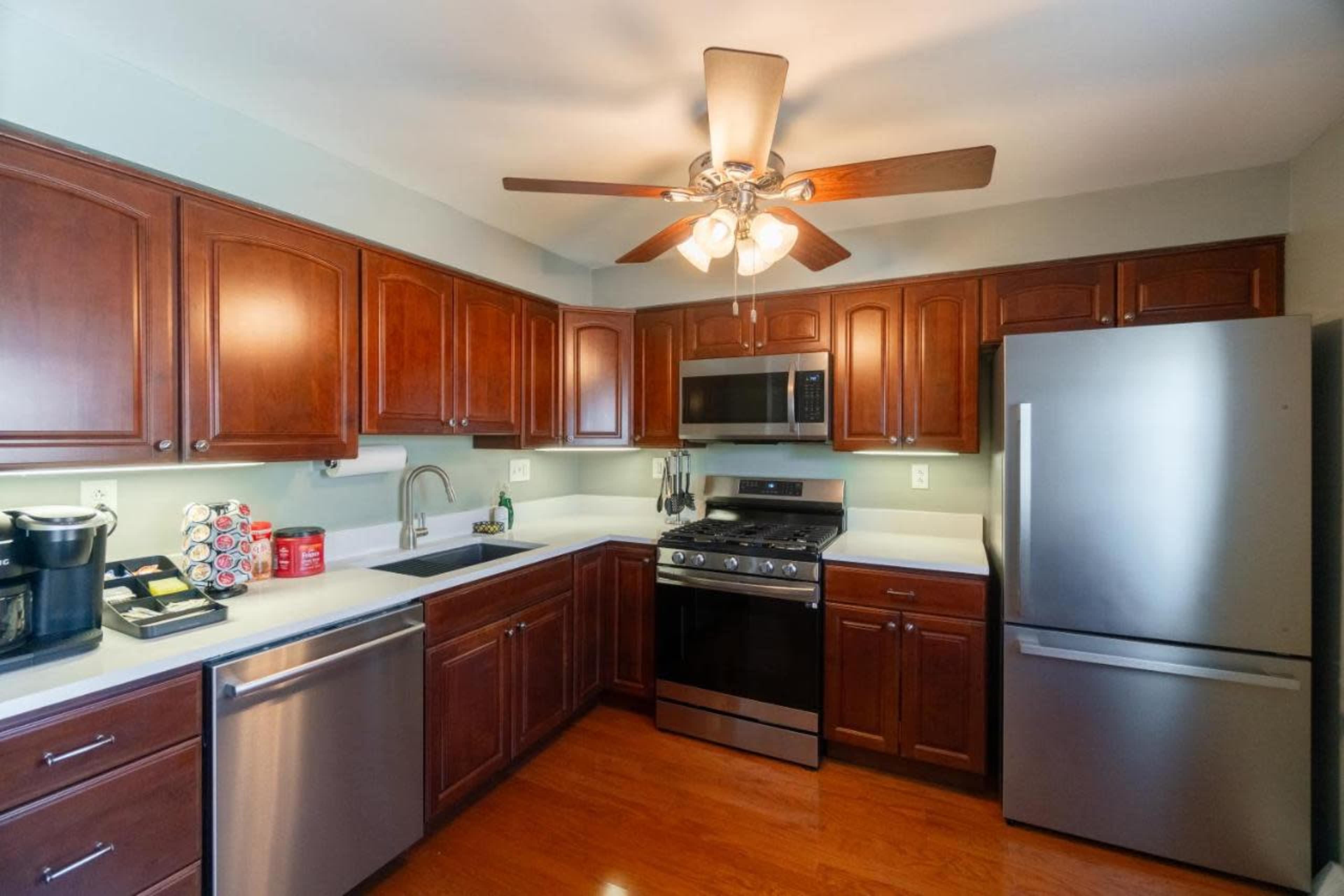 A modern kitchen features dark wooden cabinets, stainless steel appliances, and a ceiling fan.