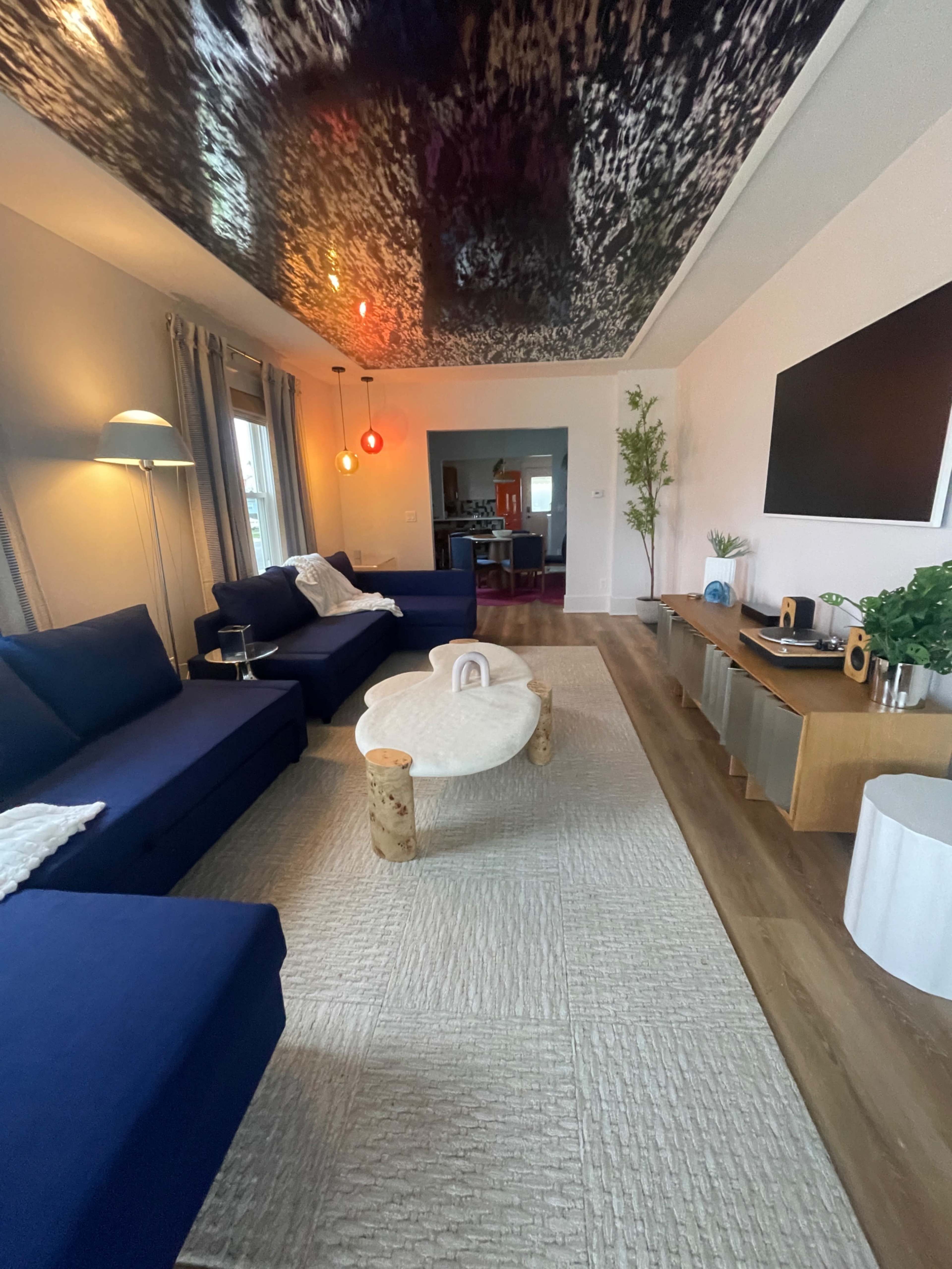 A modern living room features blue sofas, a round coffee table, and a television mounted on a wall with decorative lighting.