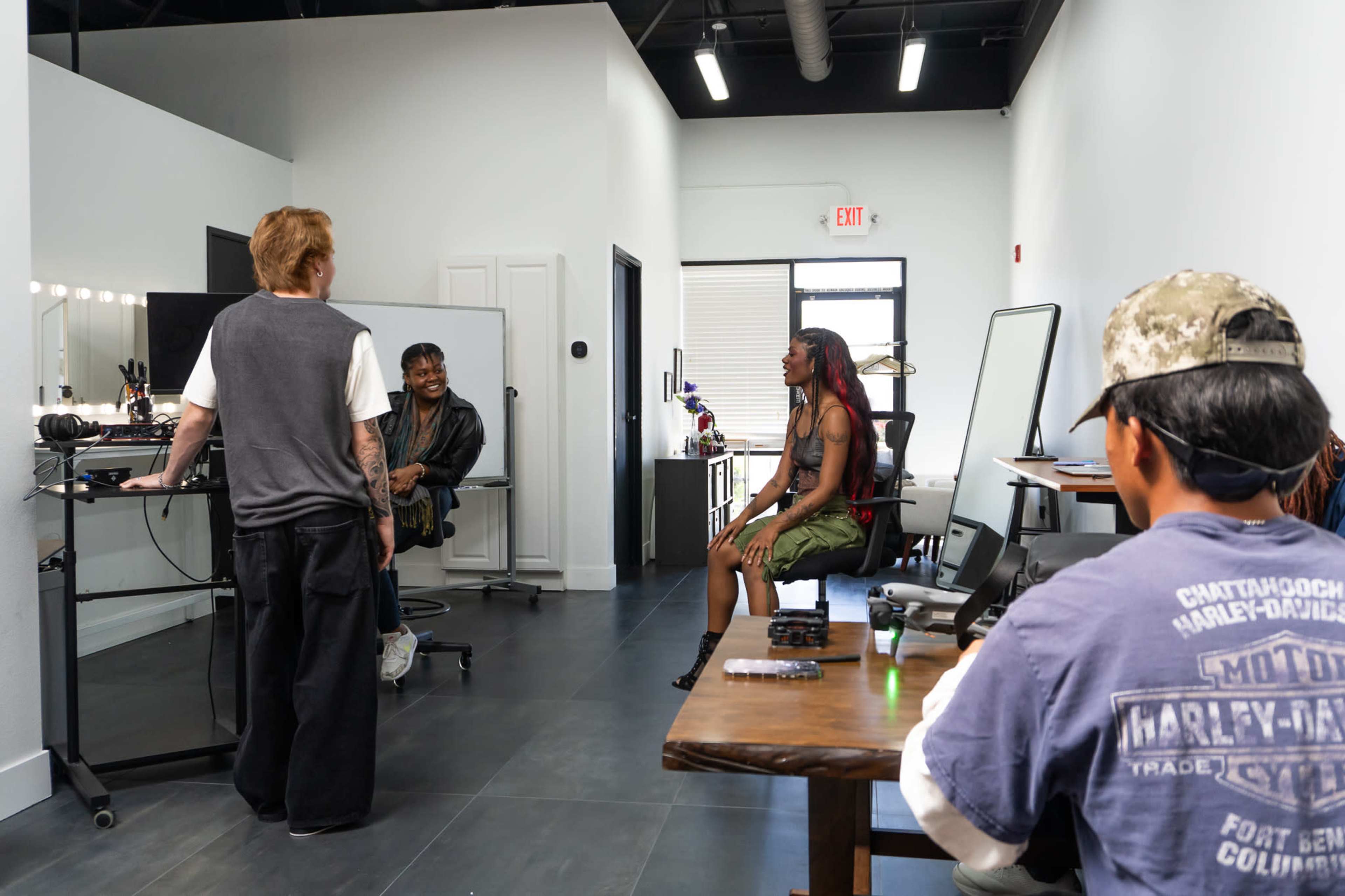 A group of four people is engaged in conversation inside a modern salon with stylish furnishings and well-lit workspaces.