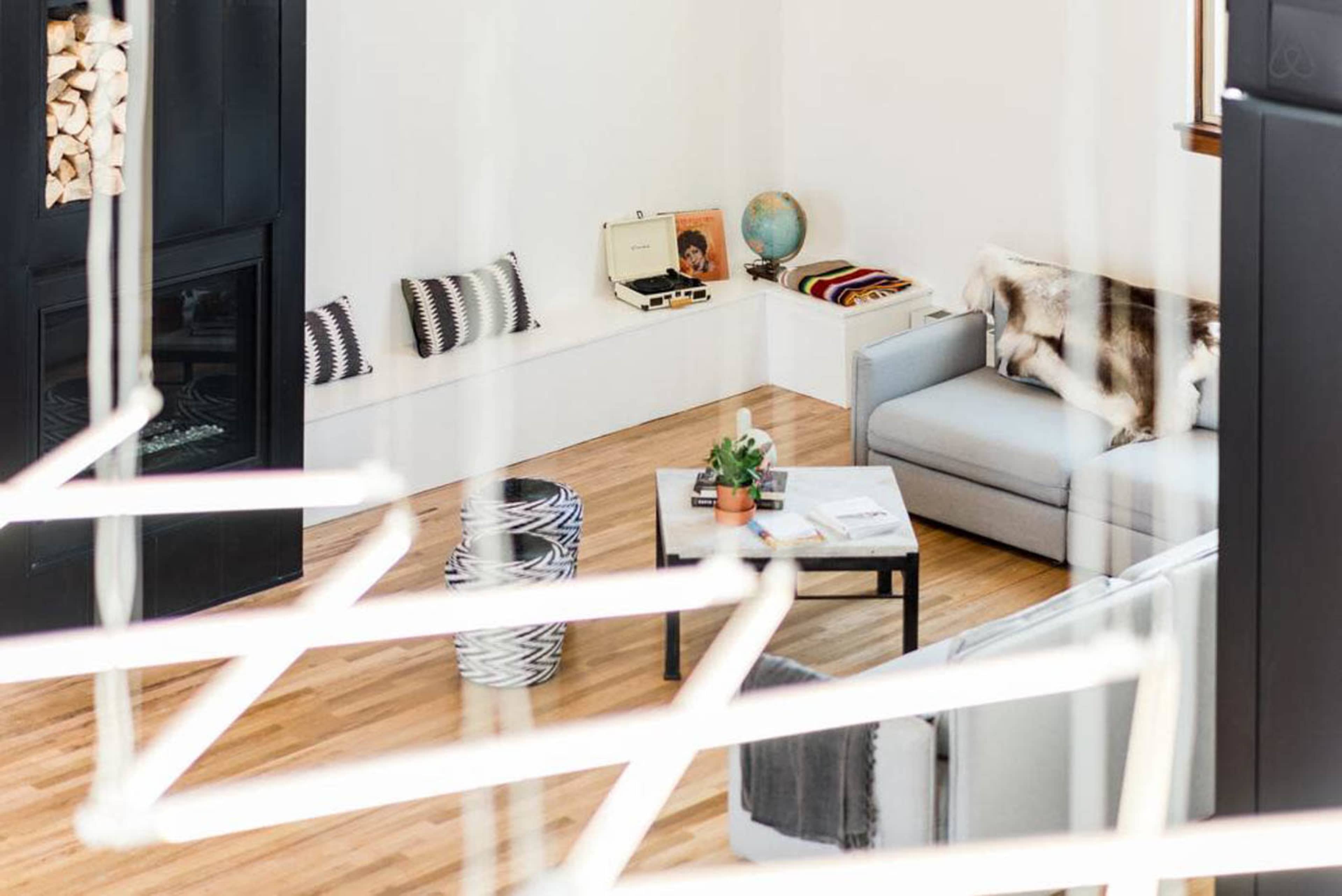 A modern living room with a gray sofa, a coffee table, a globe, a record player, and a few decorative items arranged in a light-filled space with wooden floors.
