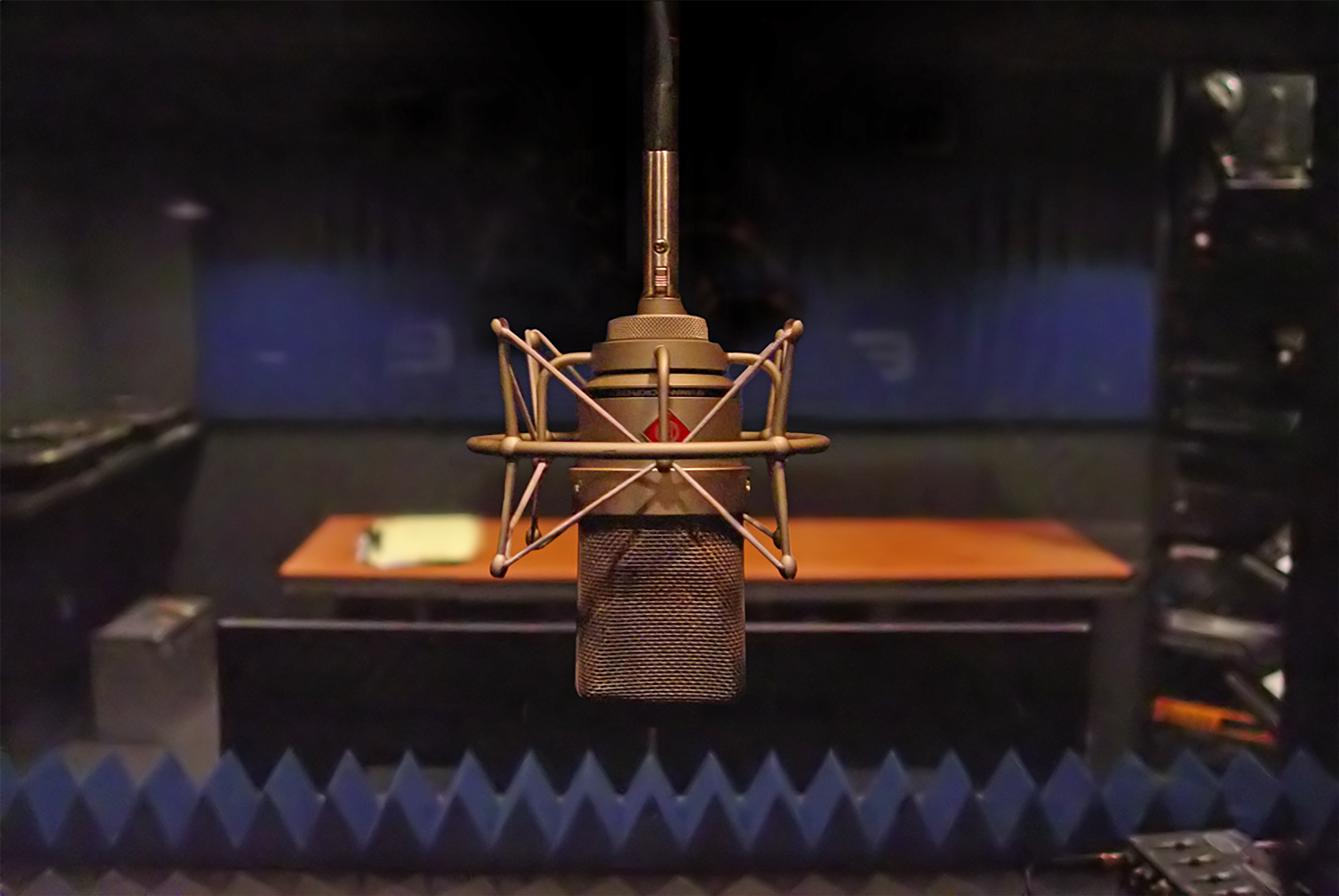A vintage microphone is positioned in a soundproof recording studio with a wooden table in the background.