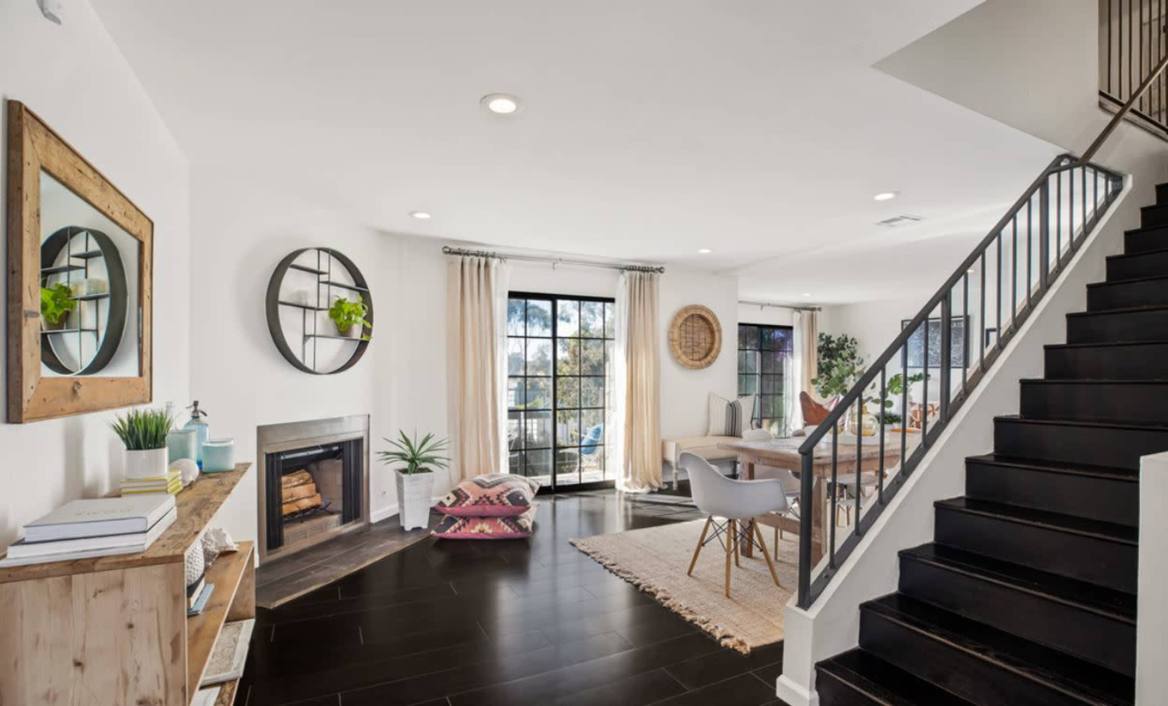 A modern living room with a fireplace, dining area, and a staircase leading to the upper level.