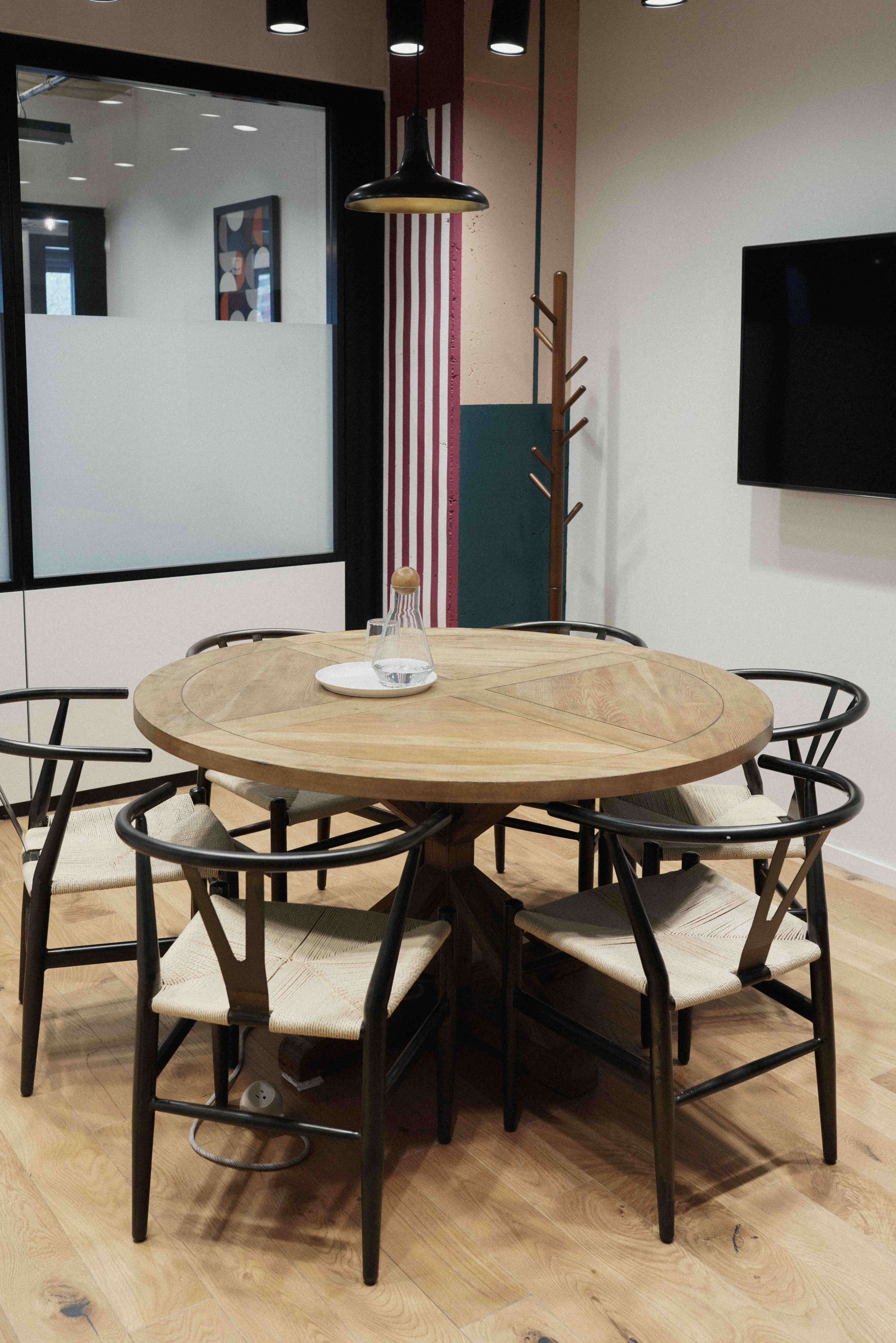 A round wooden dining table surrounded by six black and beige chairs in a modern office setting.