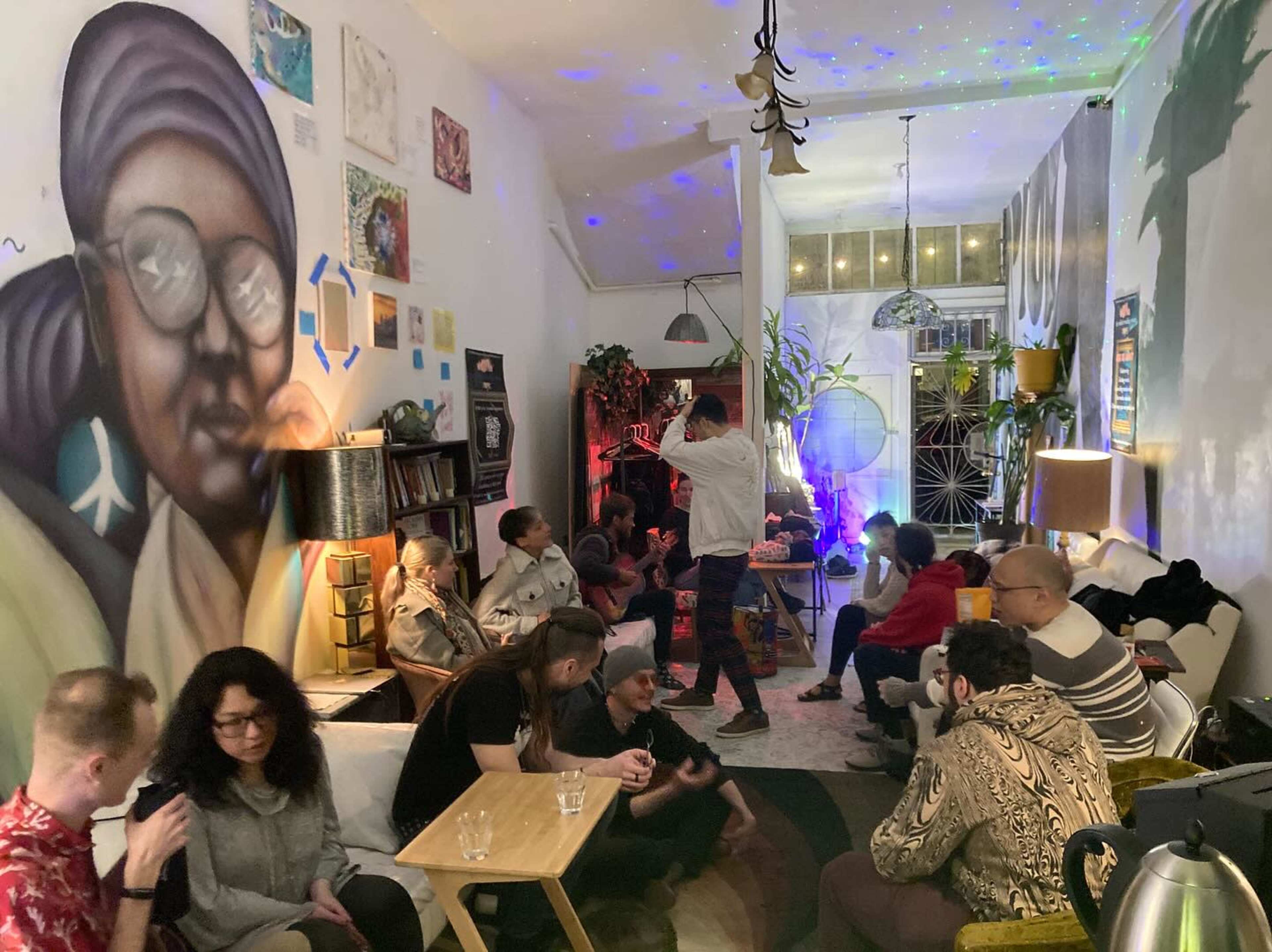 A diverse group of people socializes in a cozy lounge with a large mural and colorful lighting.