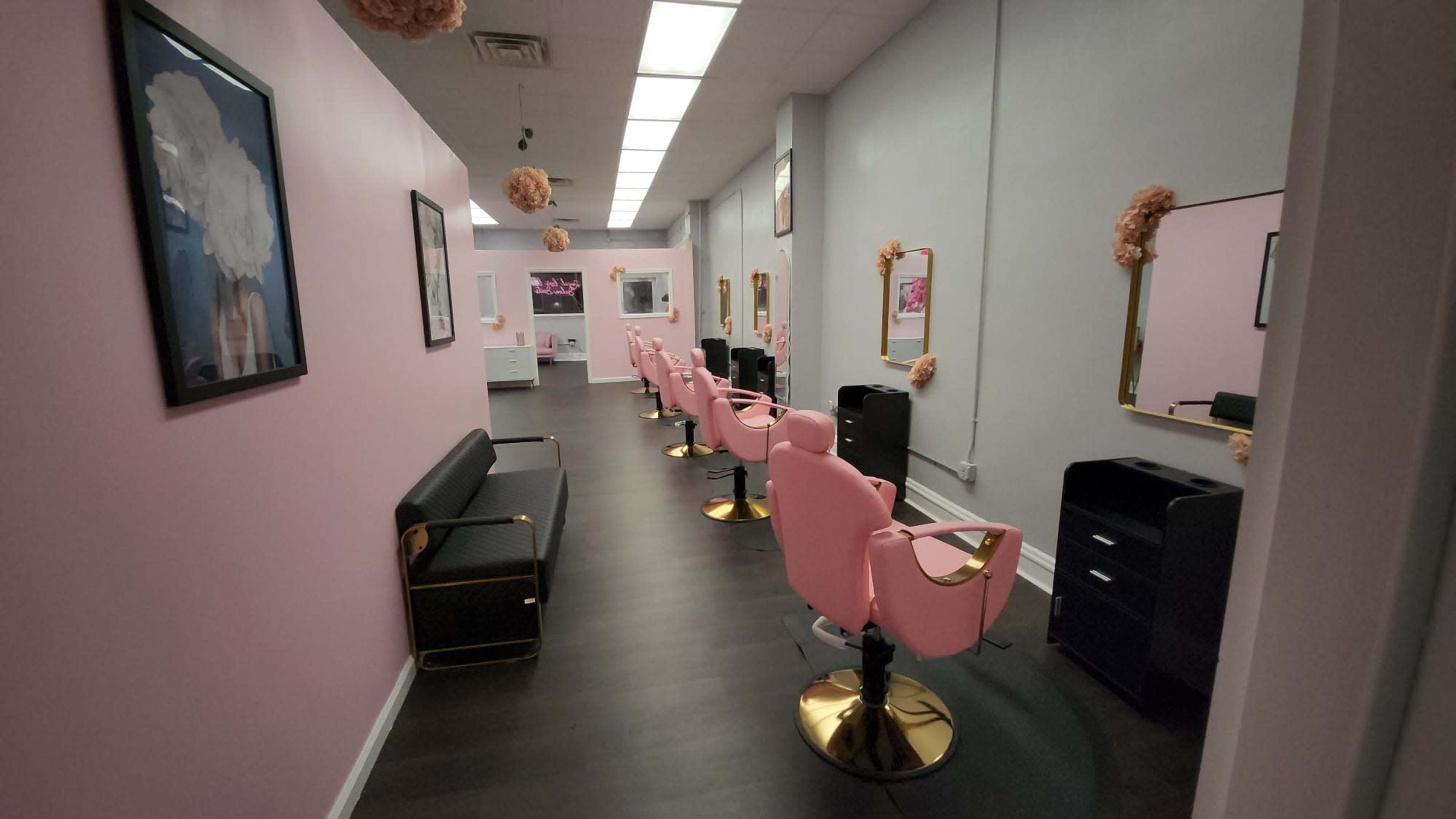 The image shows a hair salon with pink walls, black and gold furniture, and several styling chairs arranged in a row.