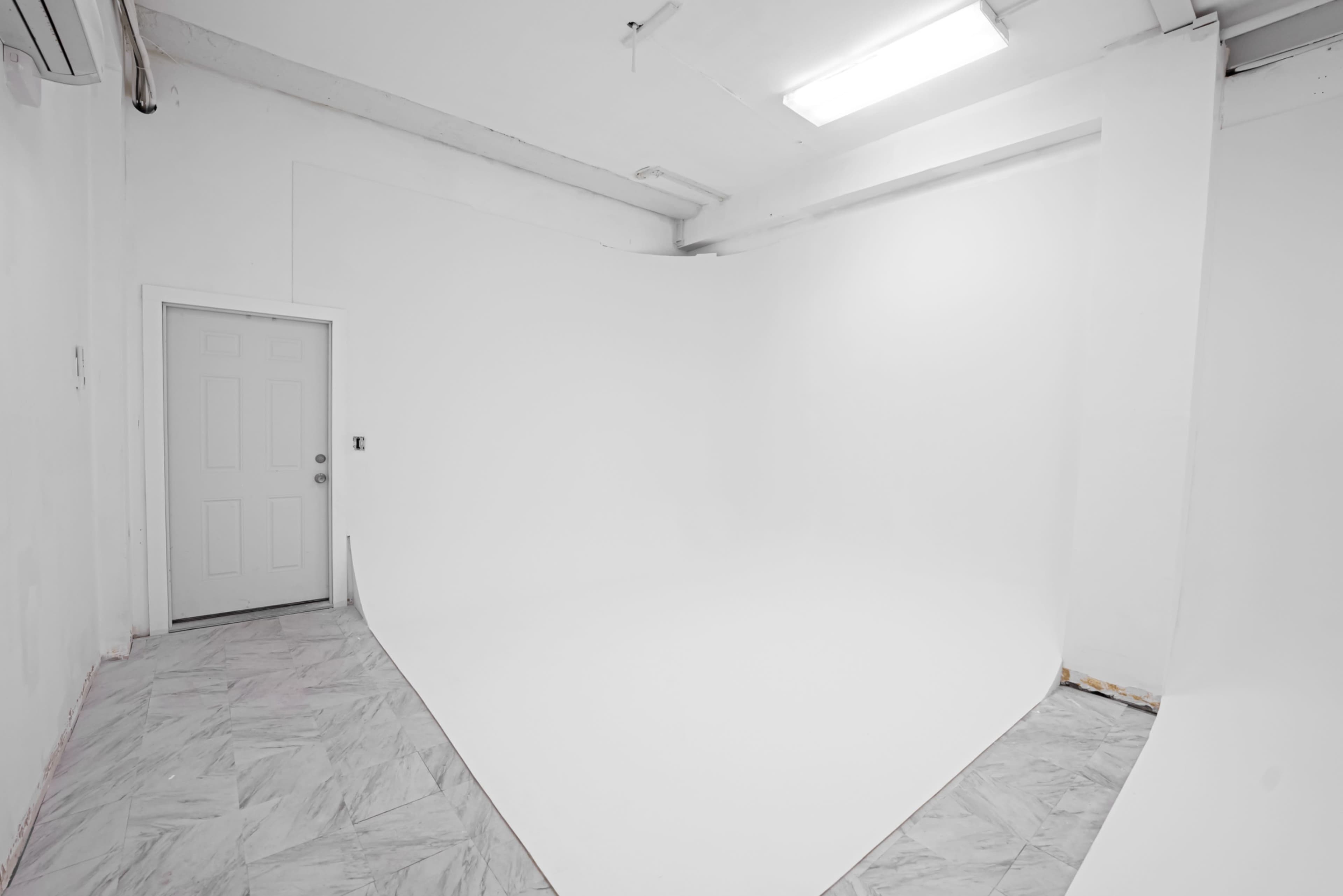The image shows a spacious, empty room with a white backdrop, a door on the left, and a marble-patterned floor.