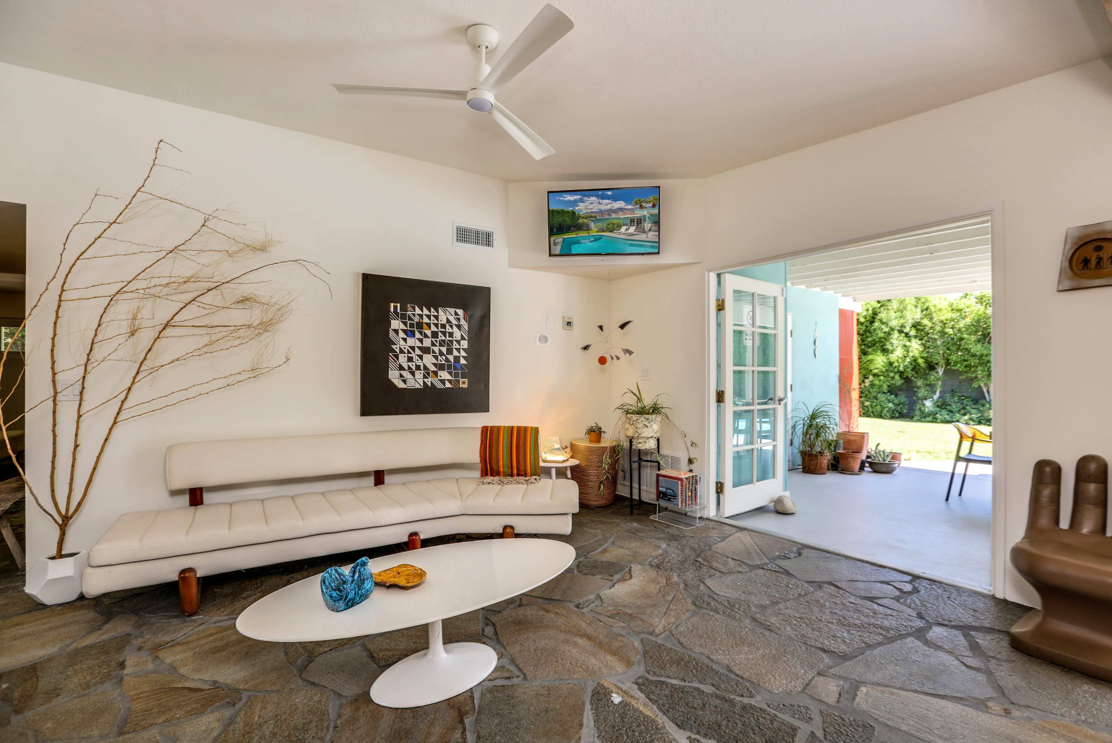 A modern living room with a white sofa, a coffee table, a stone floor, and an open doorway leading to an outdoor area.