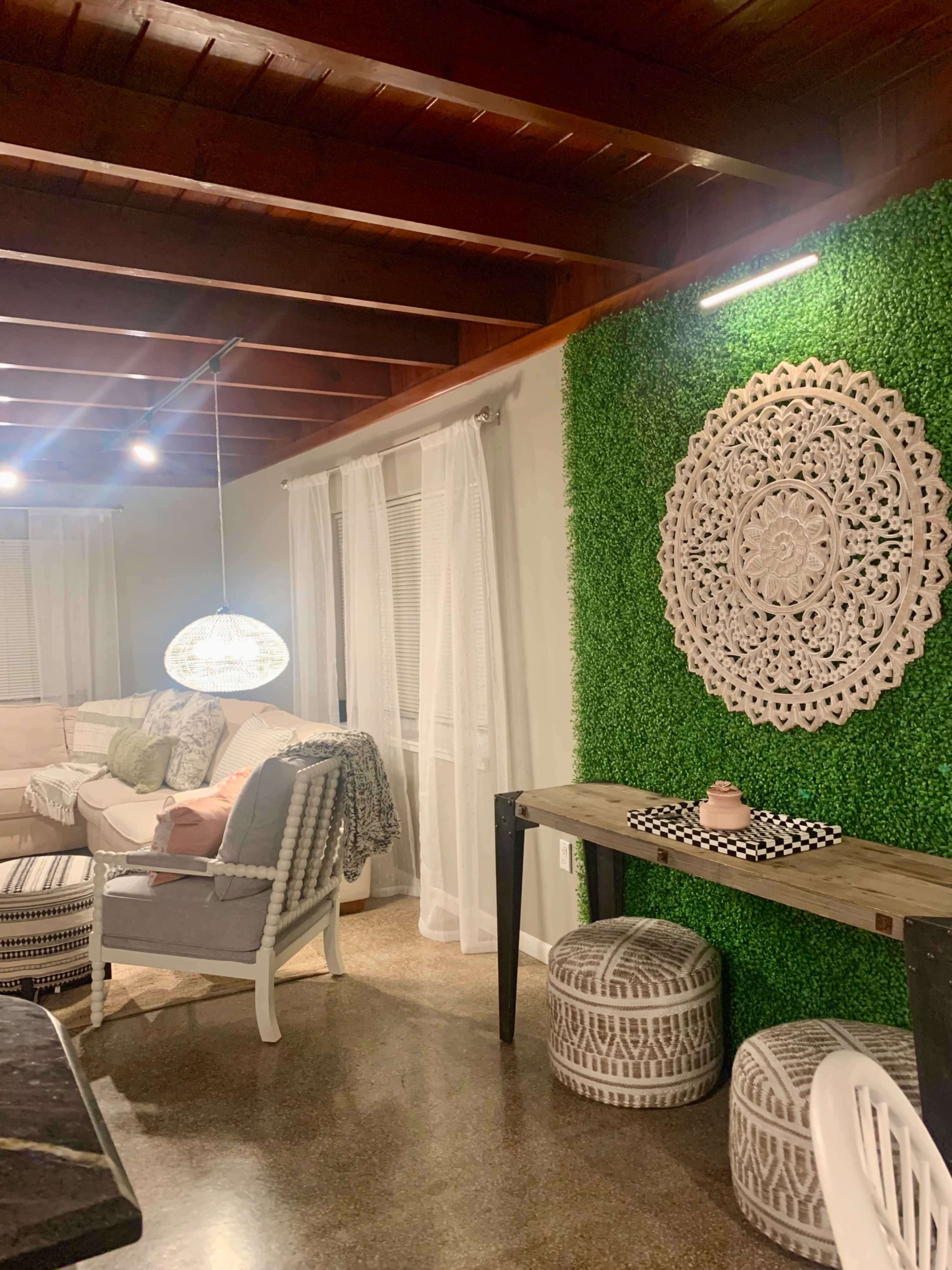 A cozy interior space features a green accent wall with a decorative round wall piece, a wooden table, and various seating options.