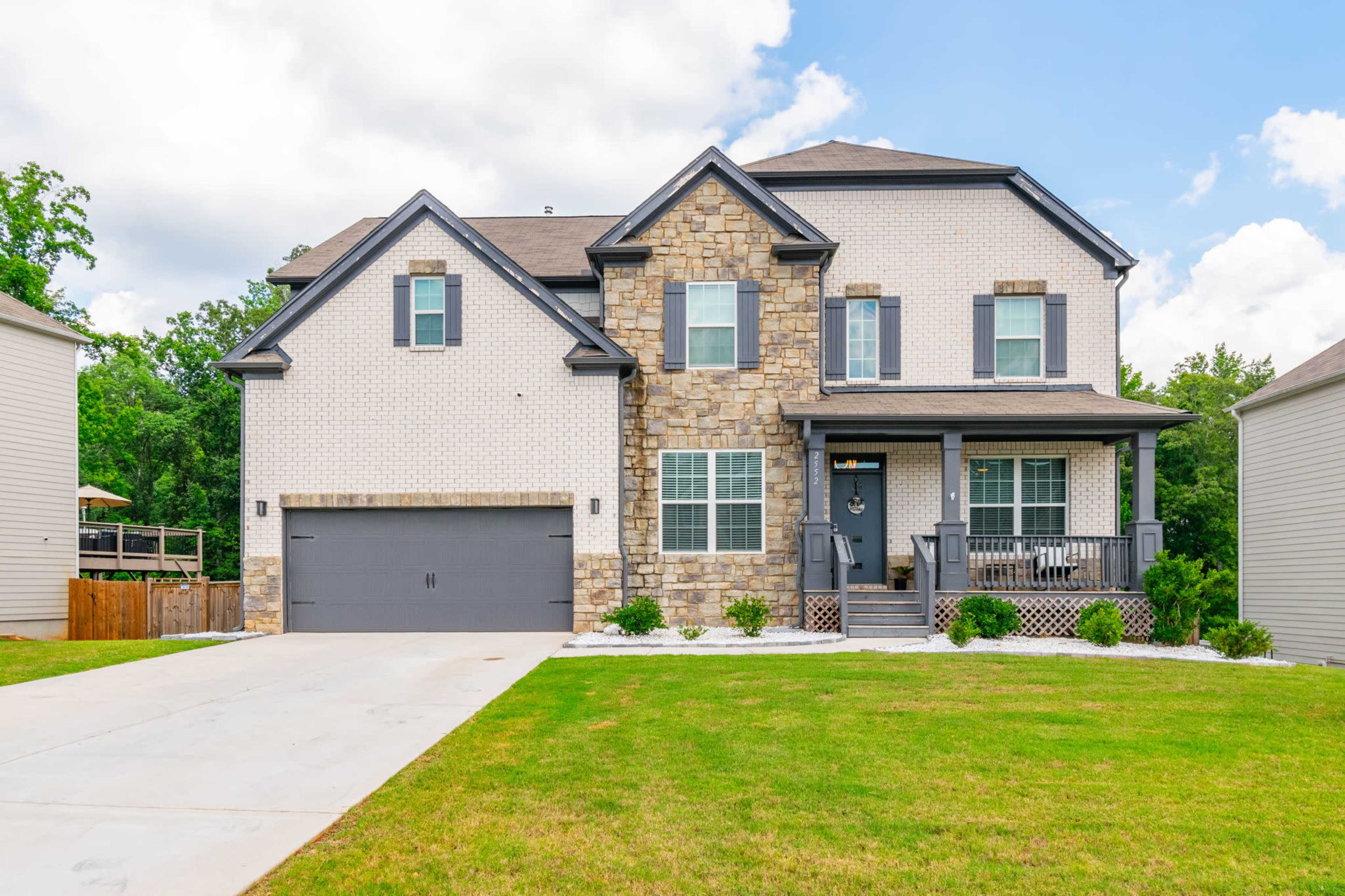 A two-story house with a stone and brick exterior, a front porch, and a double garage is situated on a well-maintained lawn.