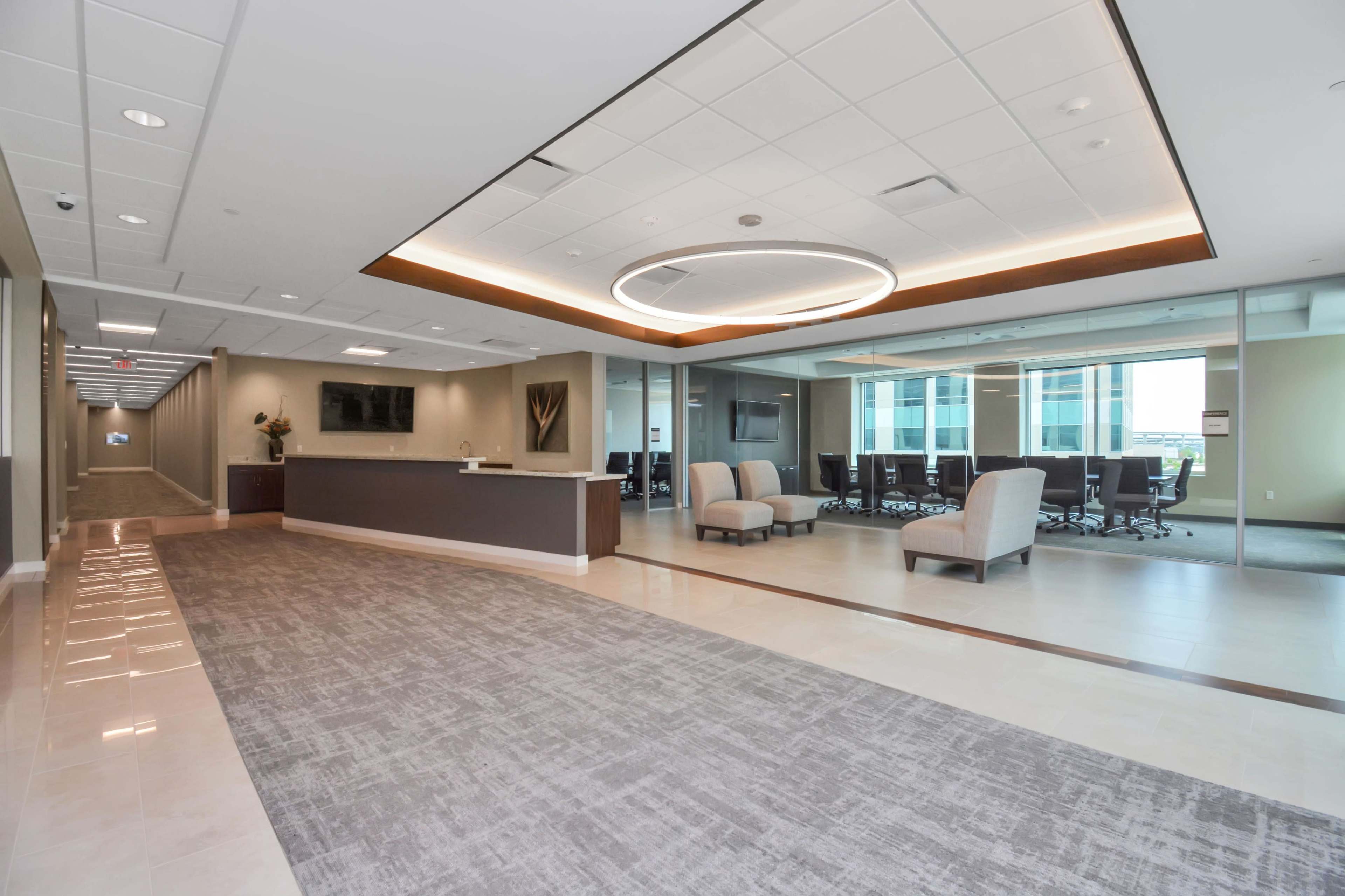 A modern office lobby with a reception area, seating space, and meeting rooms visible through glass walls.