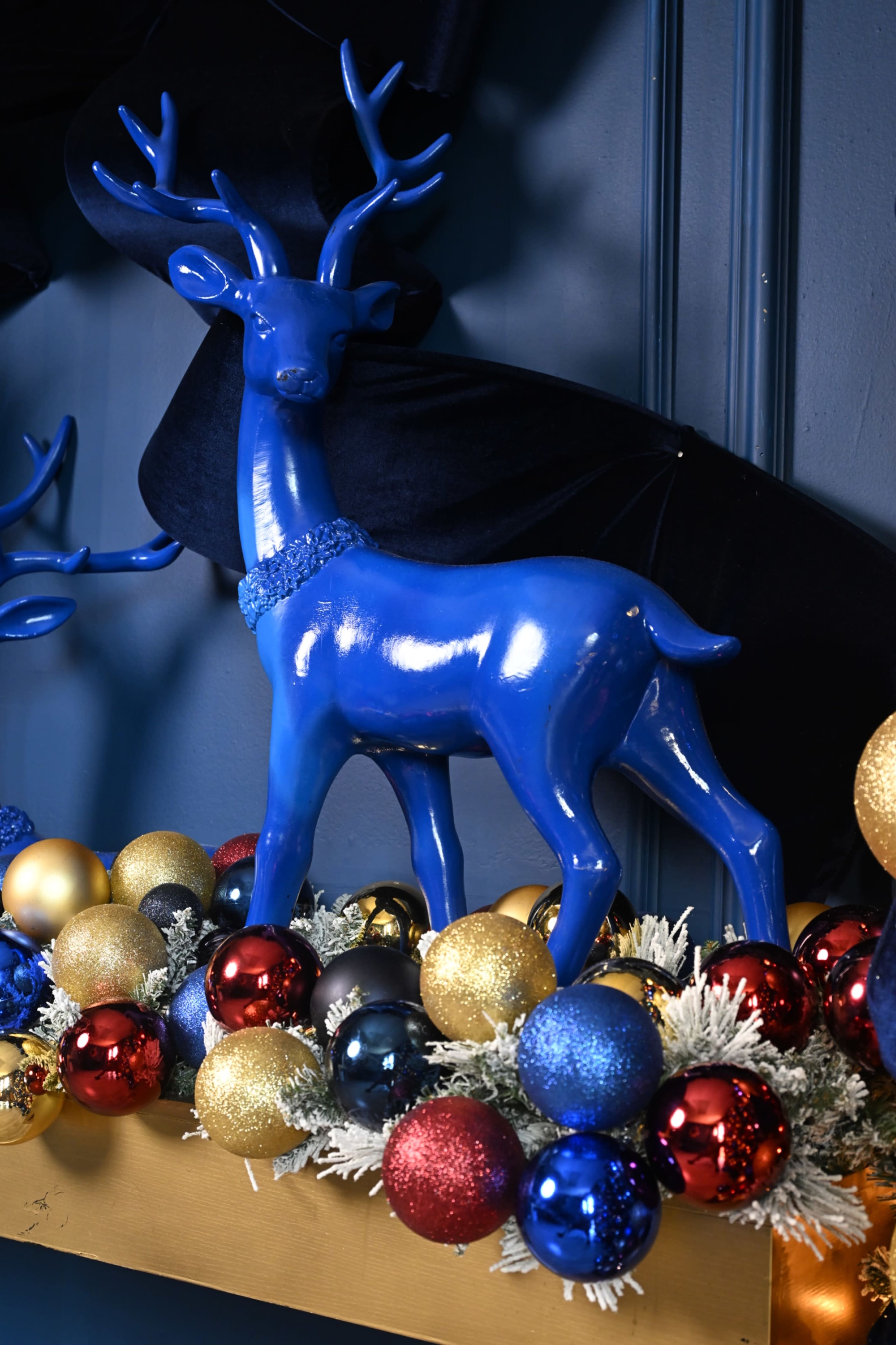 A blue decorative reindeer stands among a colorful arrangement of ornaments and garland on a shelf.