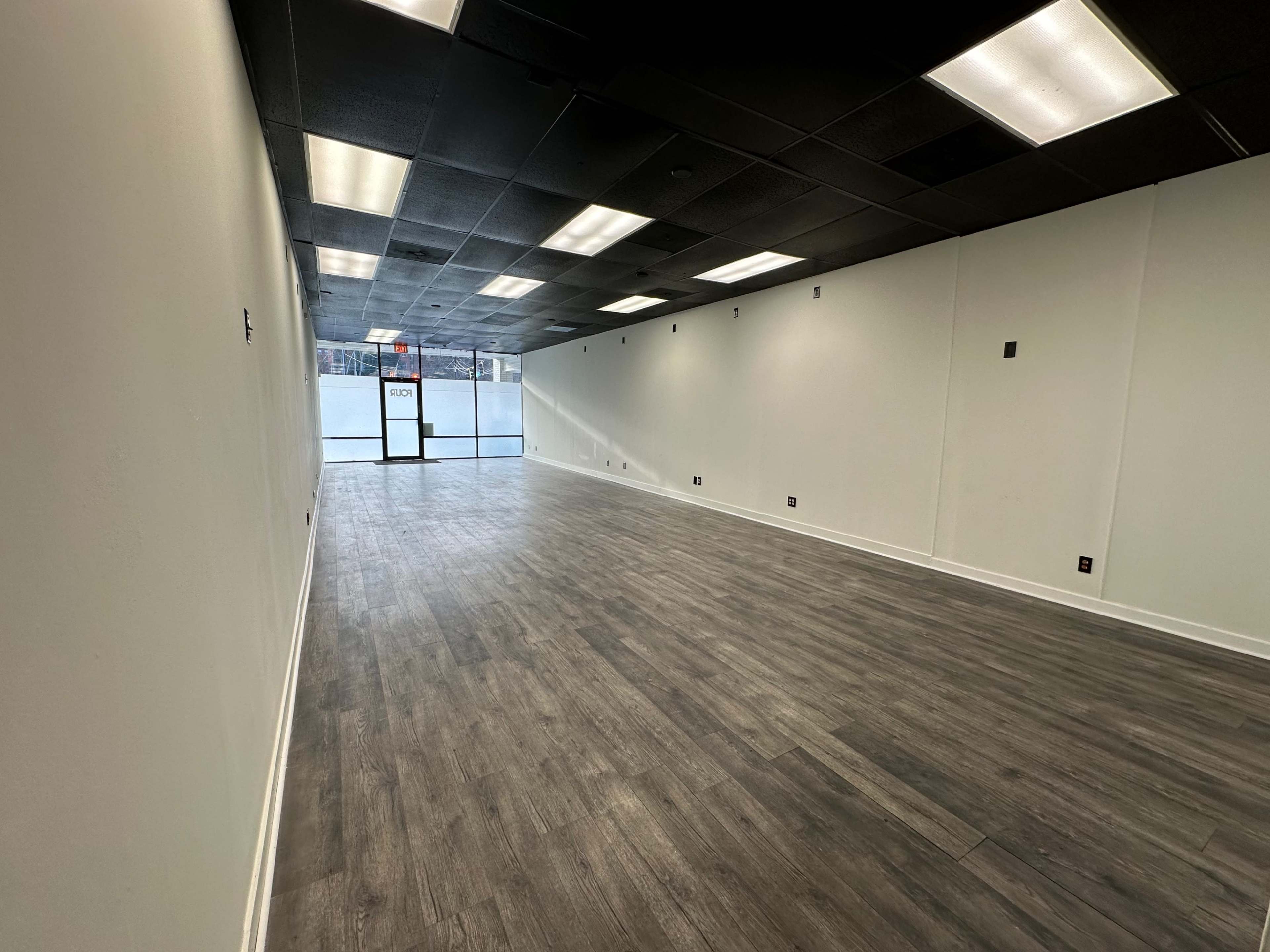 A spacious, empty interior of a retail space with laminate flooring and large windows at the entrance.