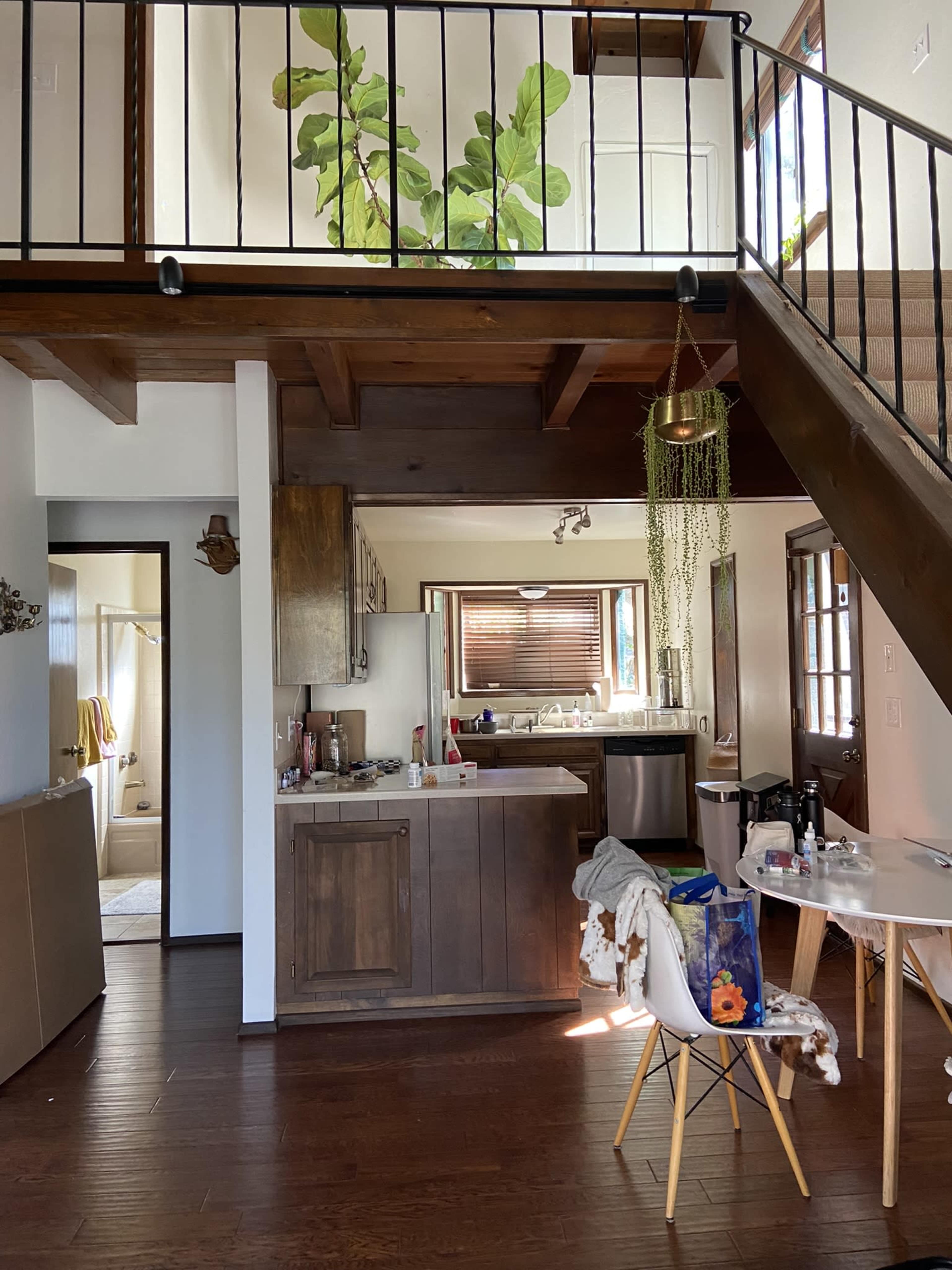 A spacious interior of a home with a kitchen and living area, featuring wood accents, a staircase, and various plants.