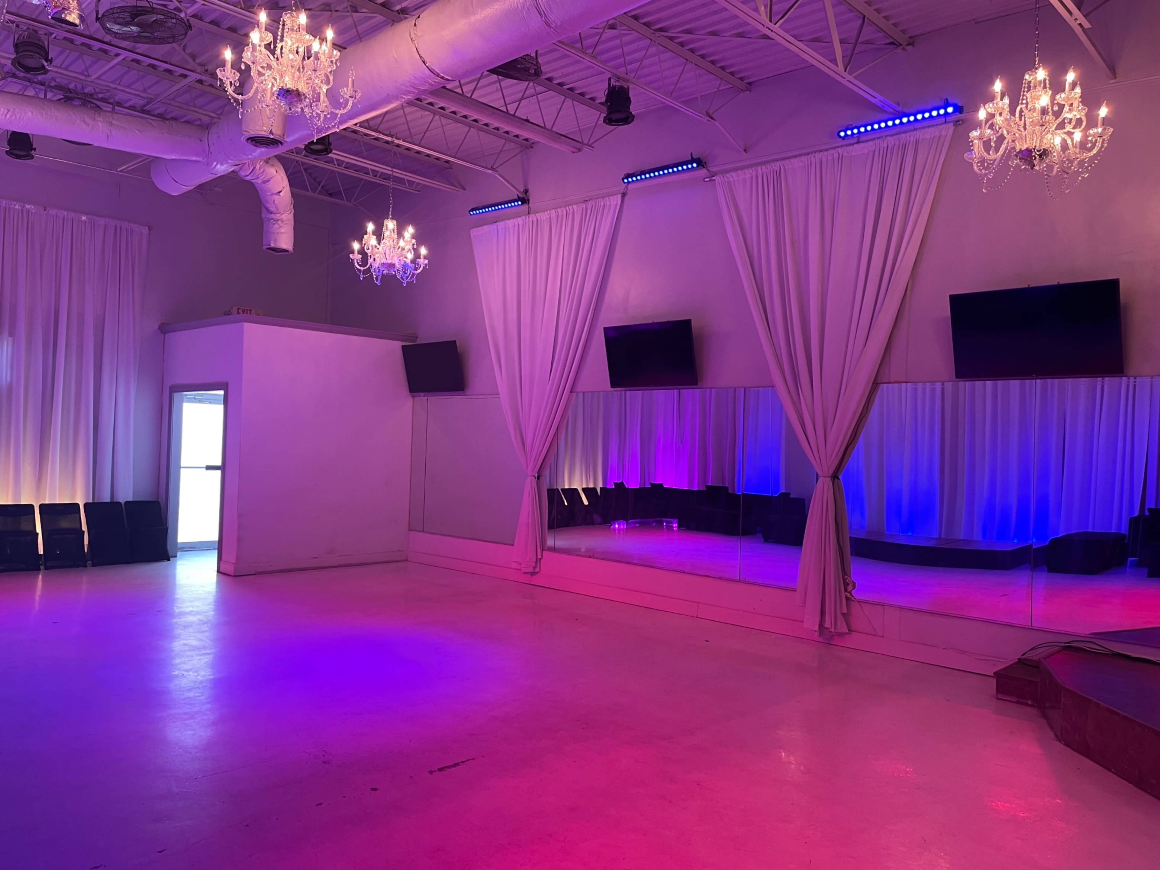 The image shows an empty event space with two chandeliers, large mirrors on one wall, and illuminated curtains in purple and blue tones.