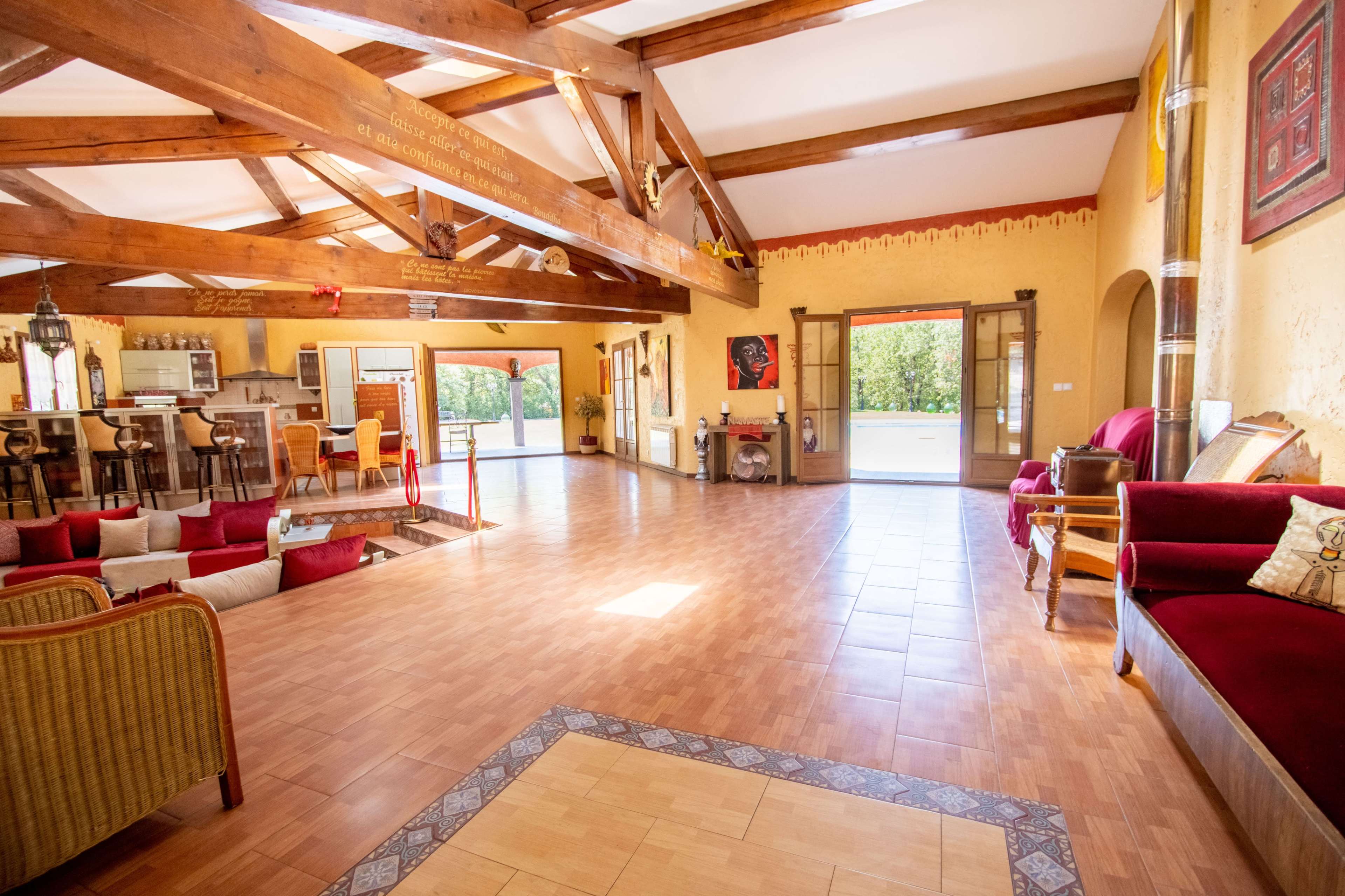The image depicts a spacious interior of a house featuring wooden beams, a large open area with tiled flooring, and a combination of traditional and modern furnishings.