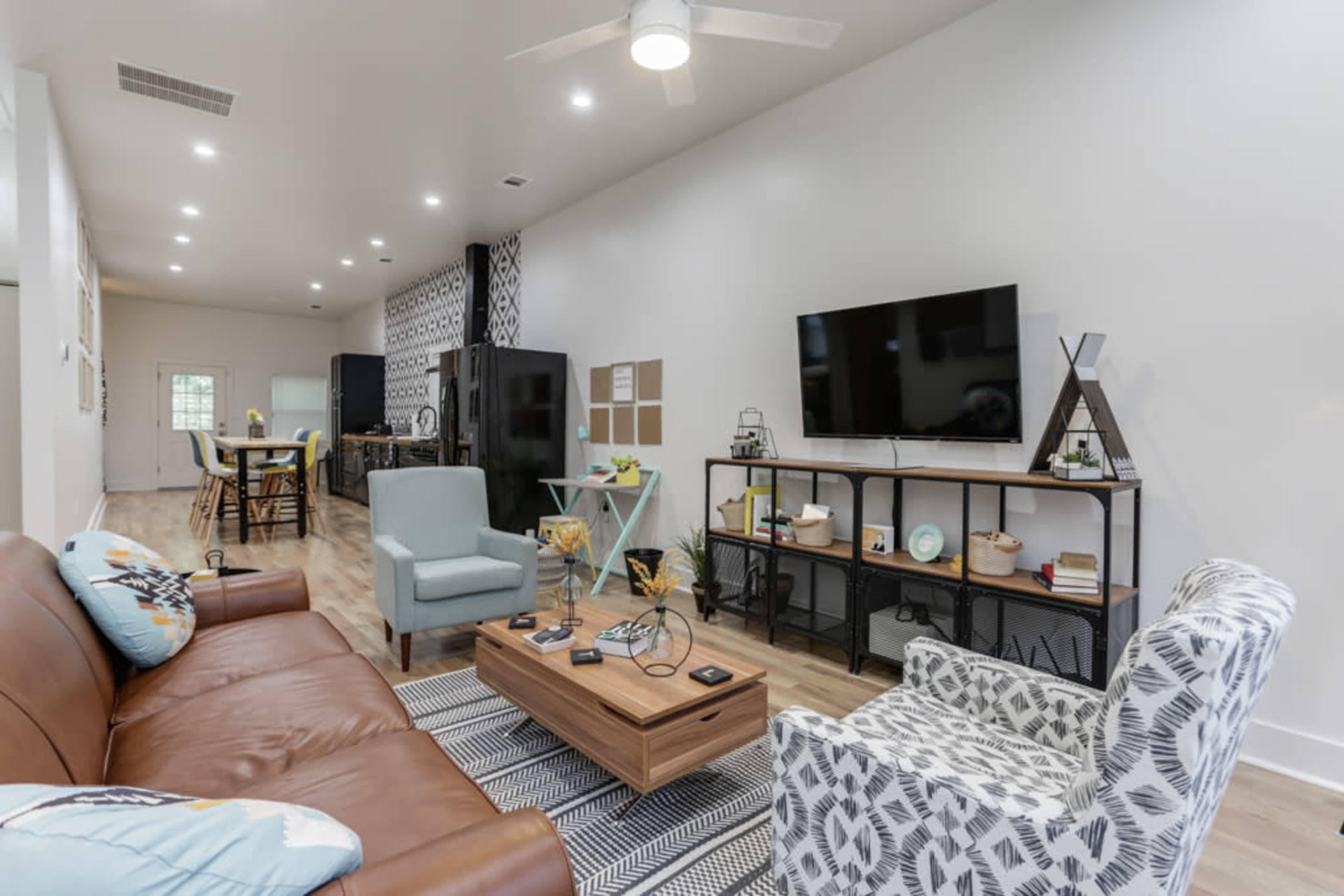 A modern living room with a brown sofa, light blue armchair, a wooden coffee table, and a wall-mounted television.