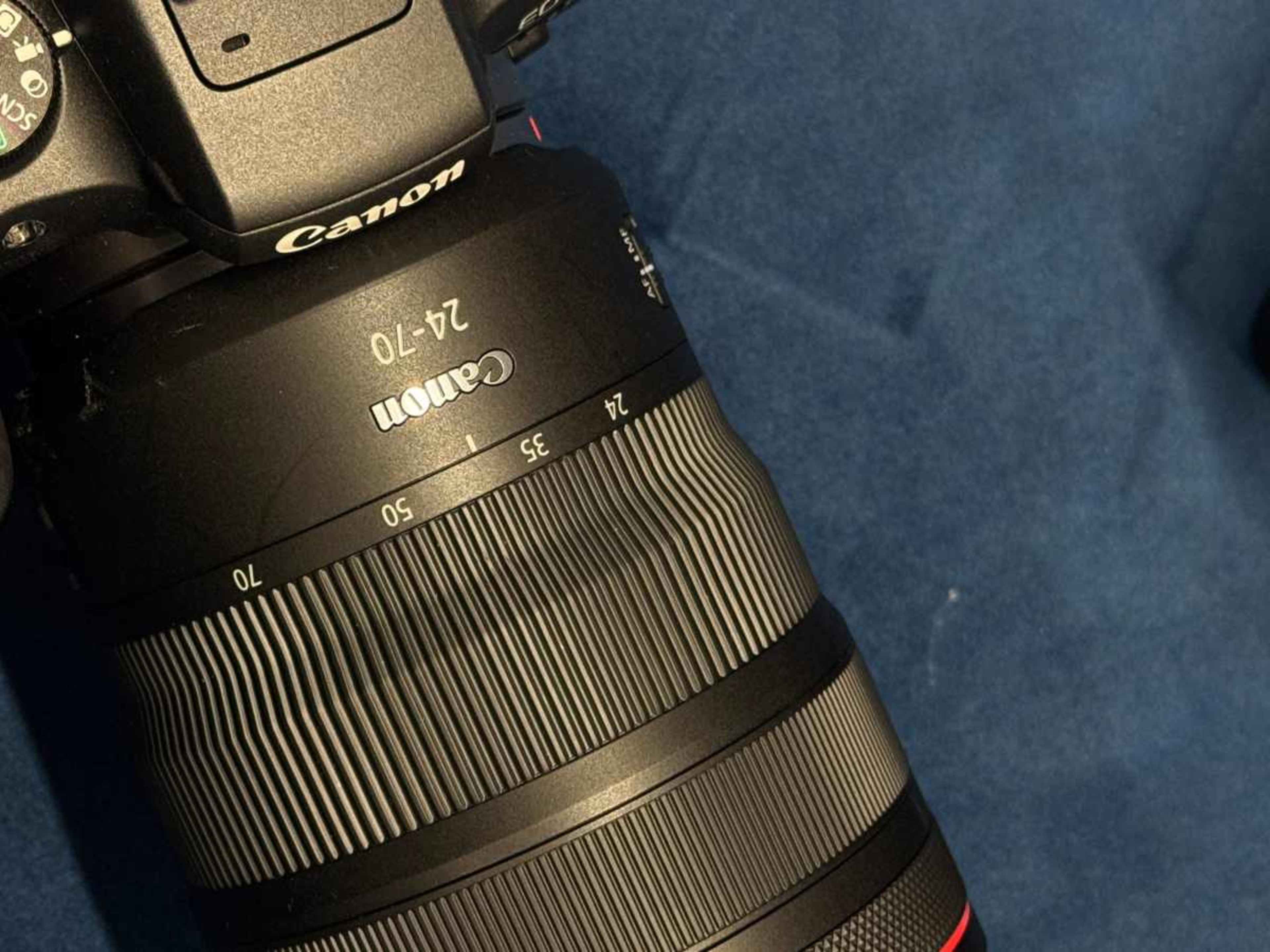 The image shows a Canon camera lens with a focal length range of 24 to 70 millimeters placed on a blue surface.